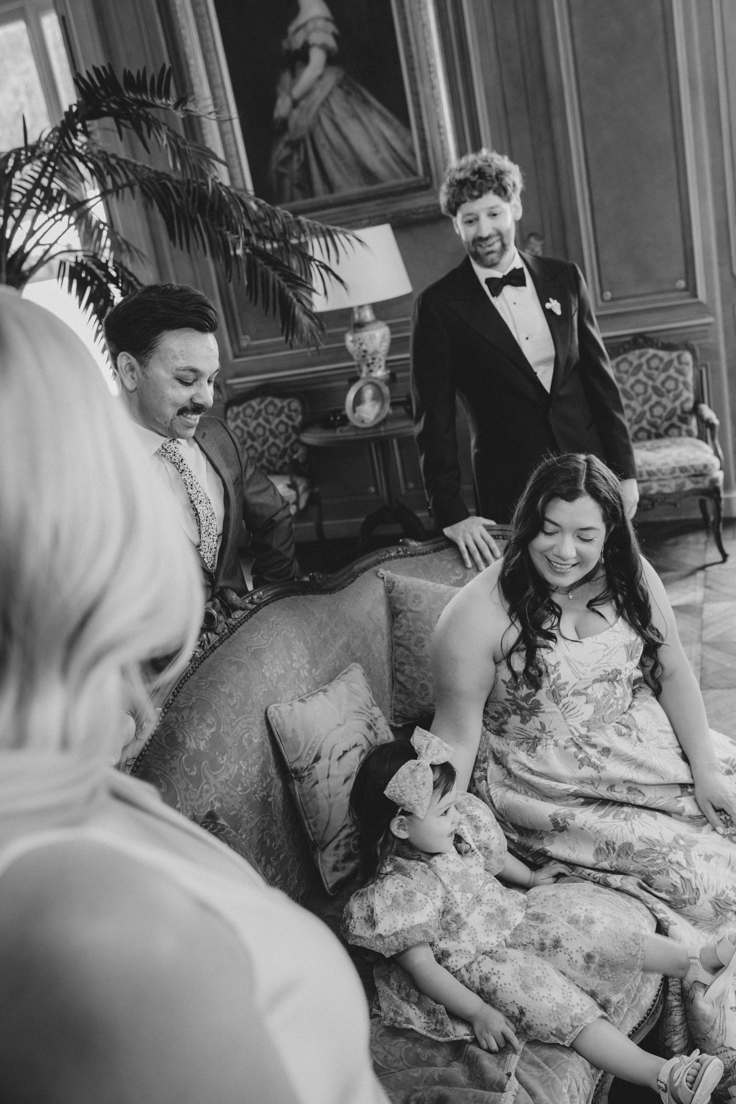 Black and white photo of wedding guests laughing and enjoying themselves on an ornate sofa.