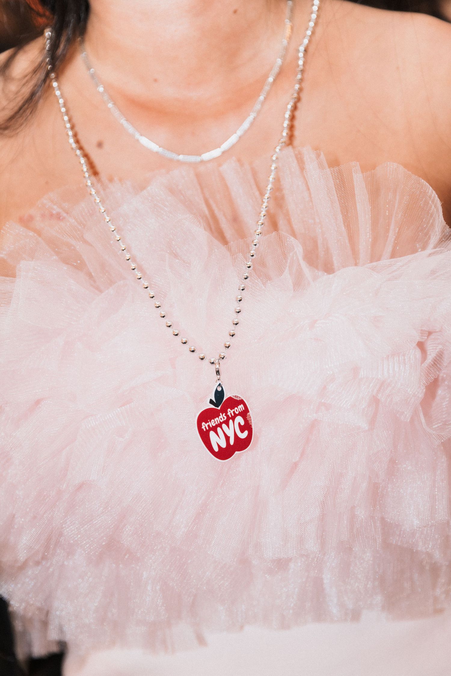 A delicate pink tulle neckline with a sparkly necklace featuring a NYC charm pendant.