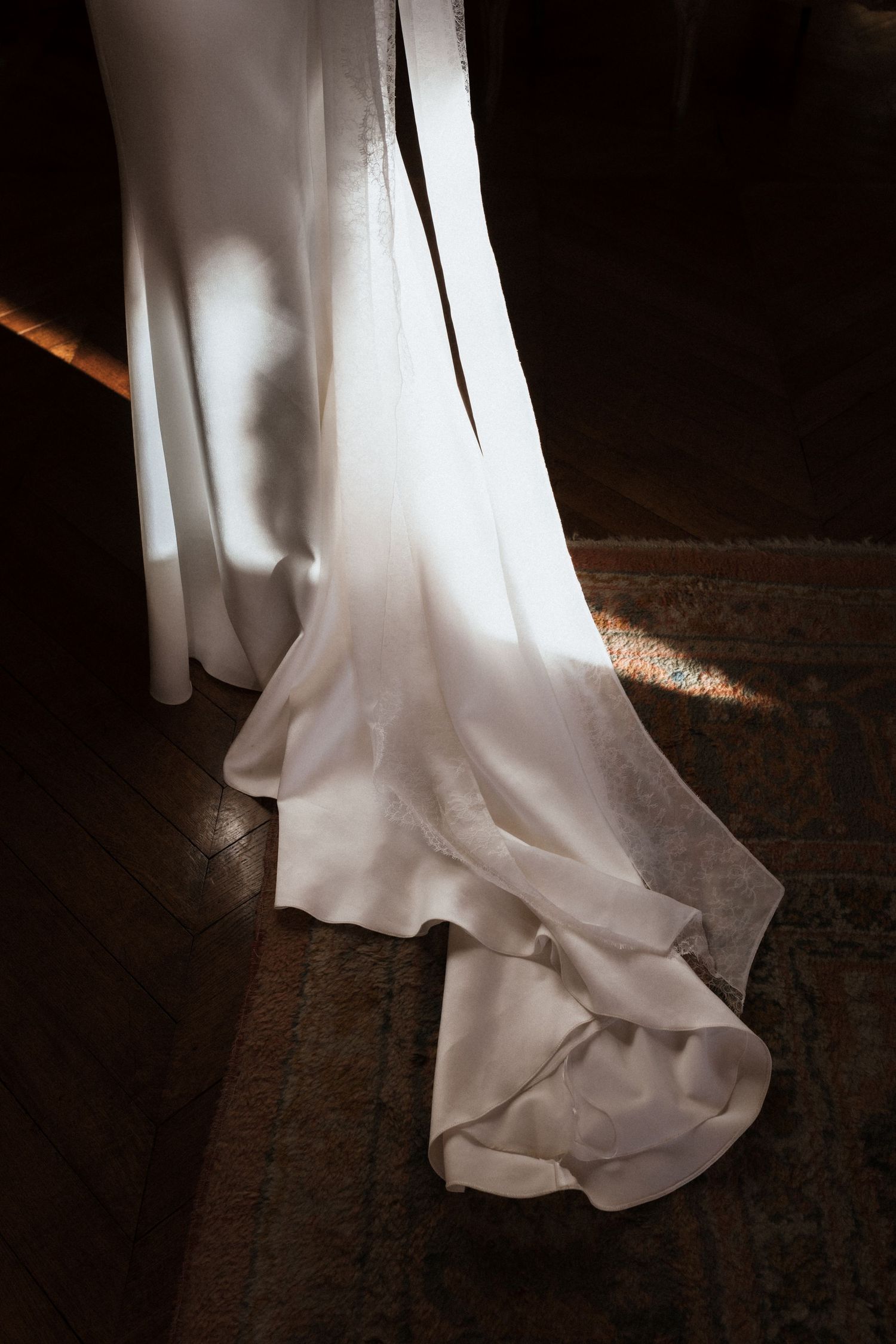 White flowing fabric drapes elegantly across dark wooden floorboards in dramatic lighting.
