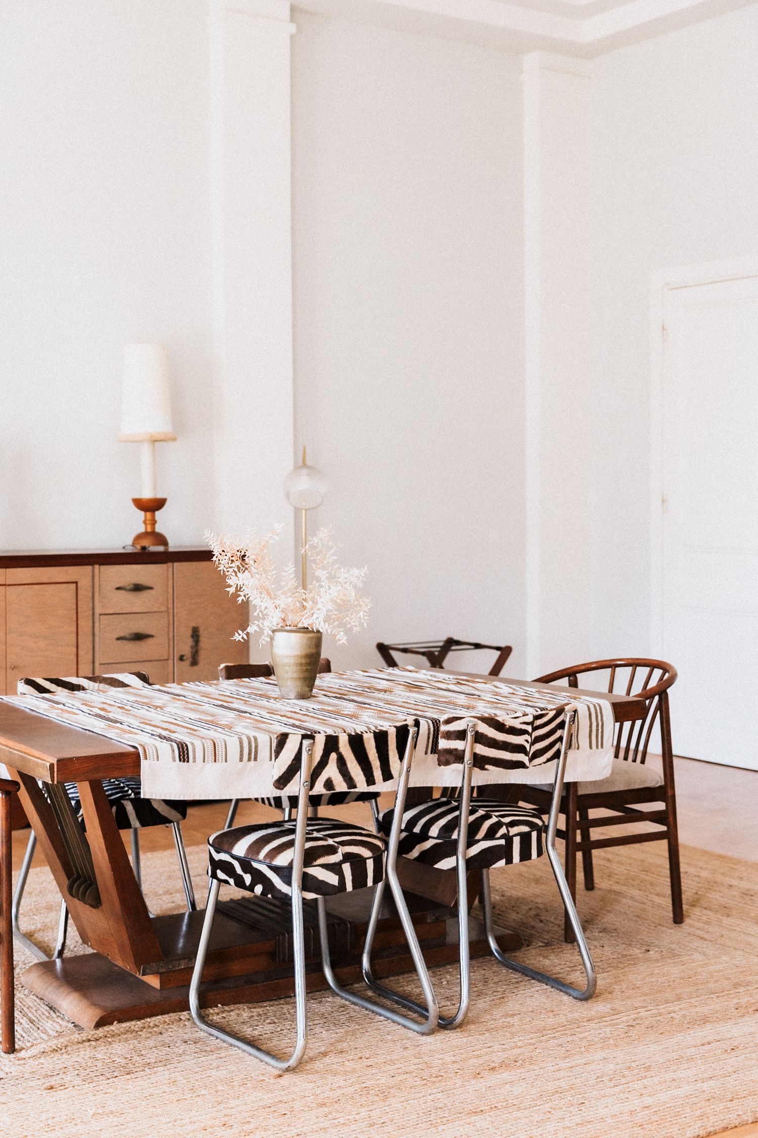 Villa Rocabella - Boho dining room with zebra print chairs, striped tablecloth, wooden sideboard, and neutral tones on a jute rug.