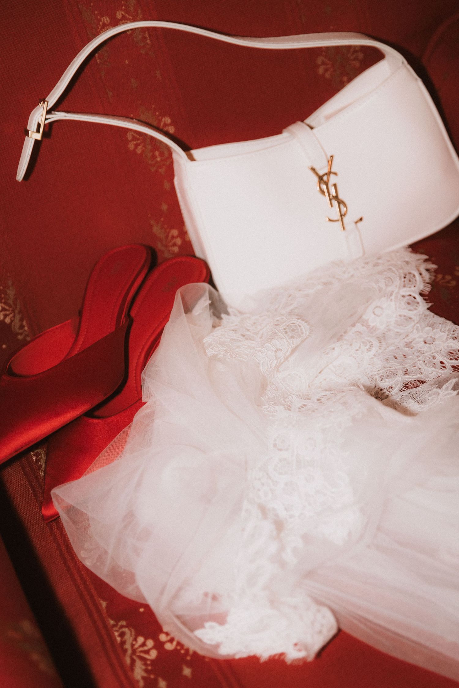 White tulle wedding dress with delicate lace details displayed against a deep red background.
