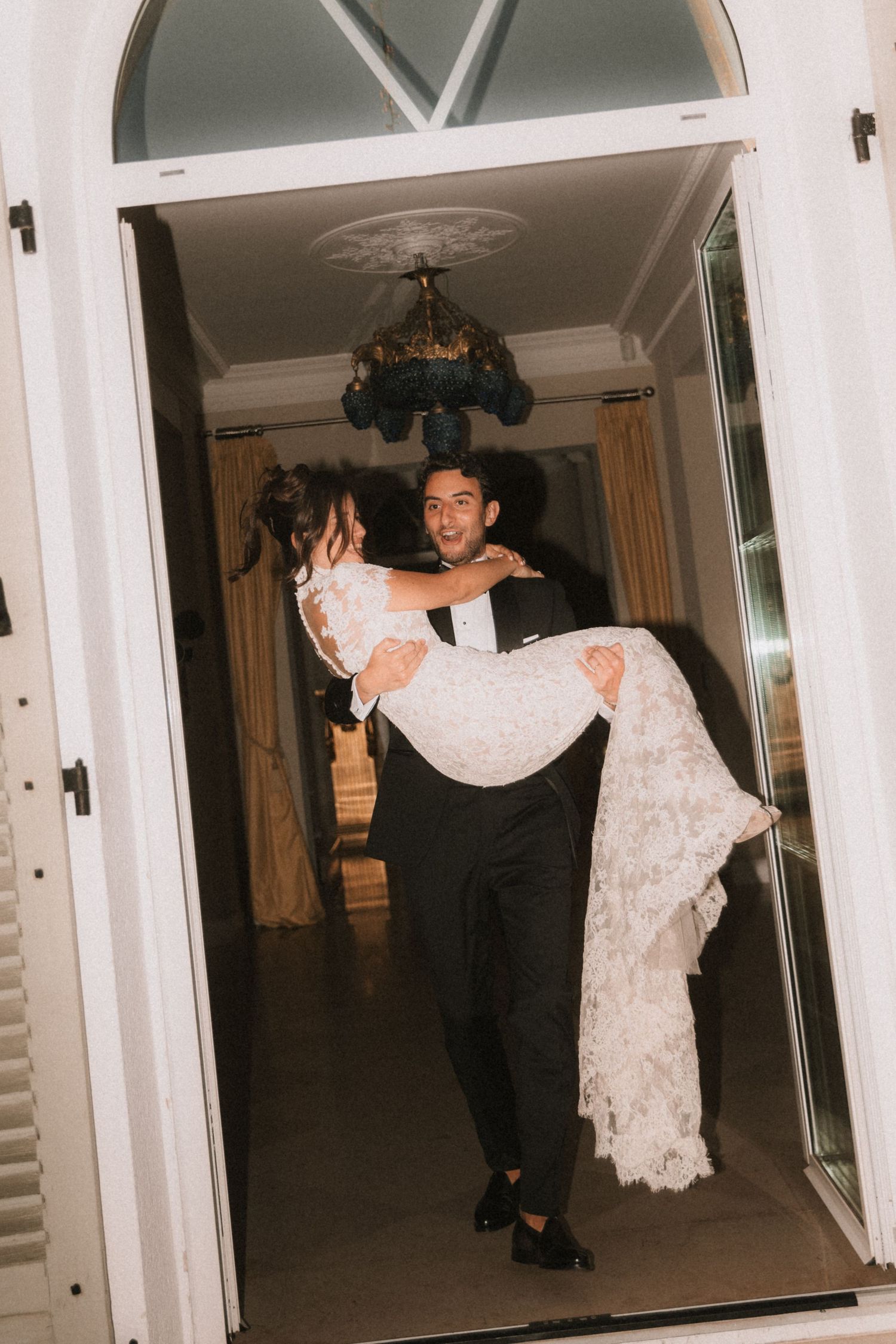 A traditional threshold carry moment through an arched doorway during a wedding celebration.