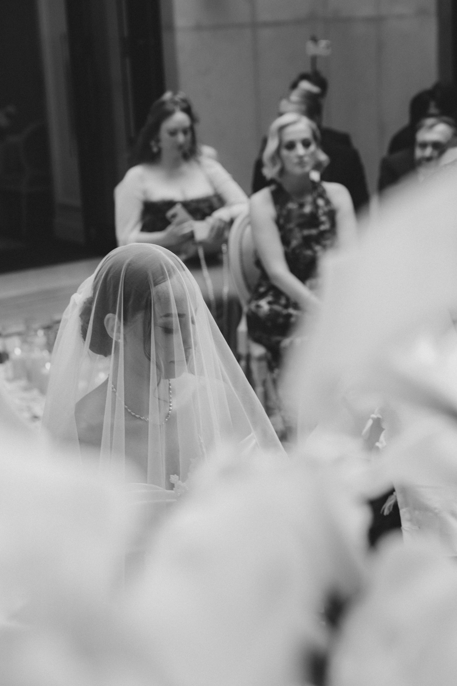 White floral arrangements frame a soft-focus view through a wedding ceremony veil.