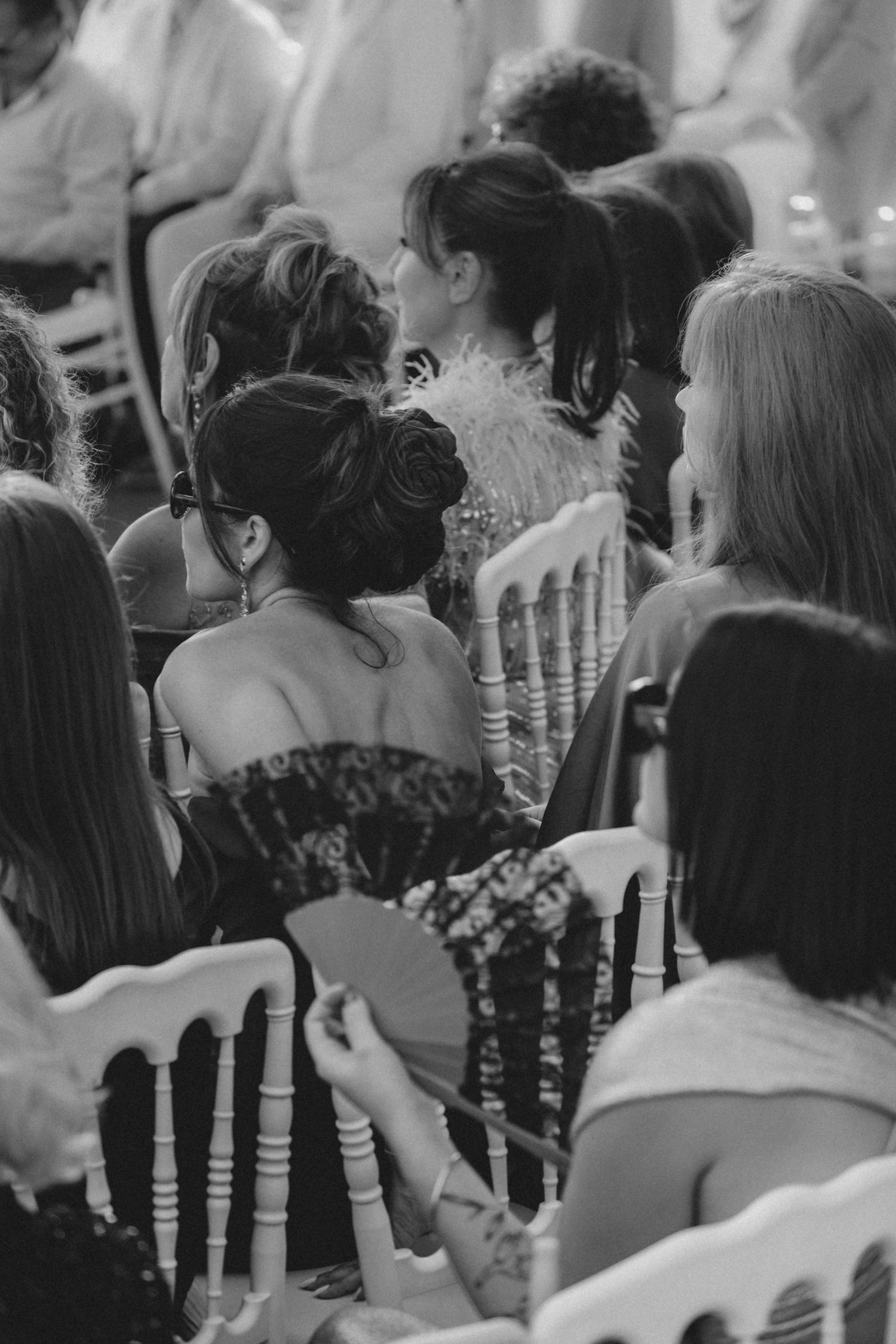 Black and white candid shot of wedding ceremony guests seated in rows with decorative aisle details.