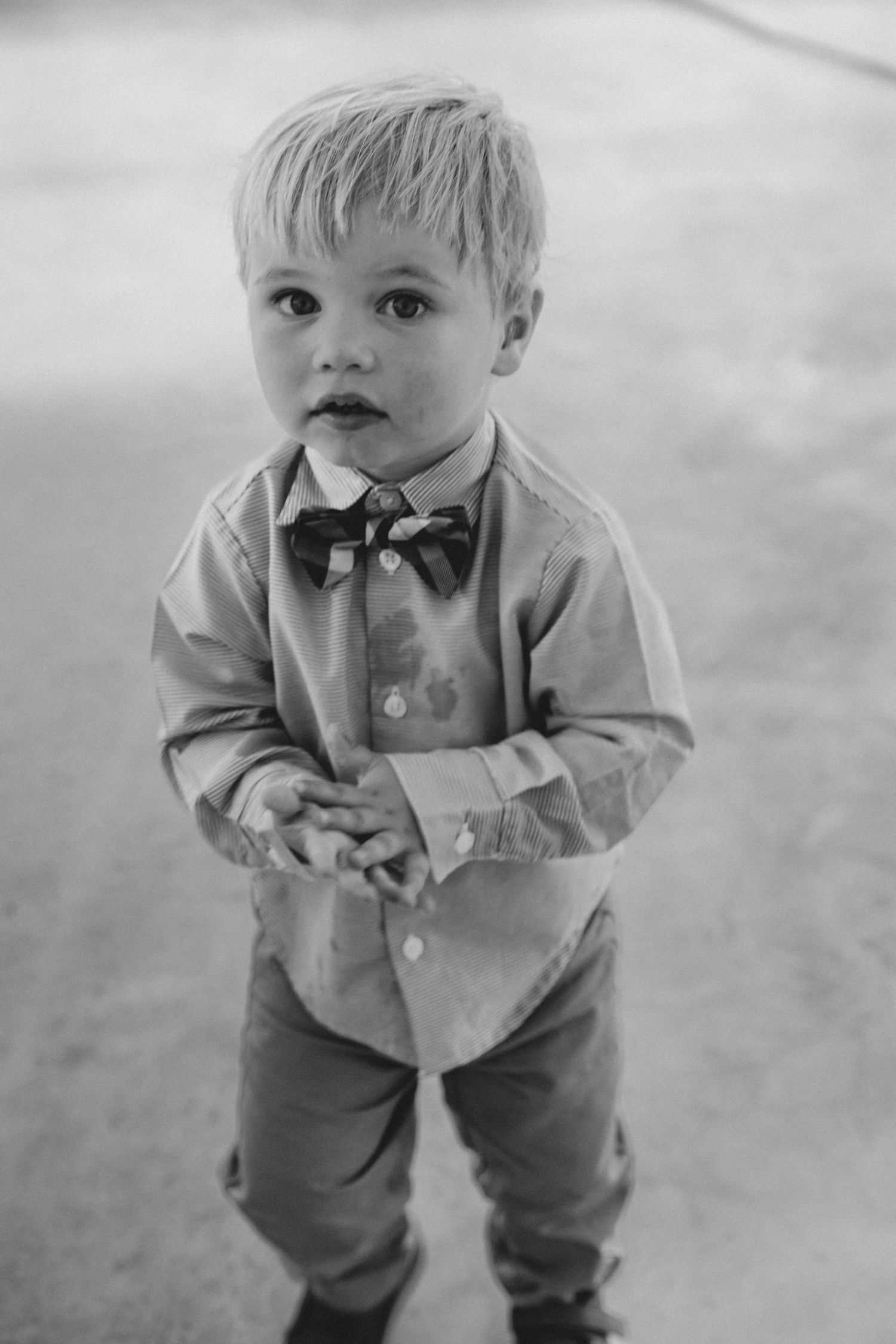 Black and white photo series showing a toddler in formal attire with a bow tie and dress shirt looking upward.