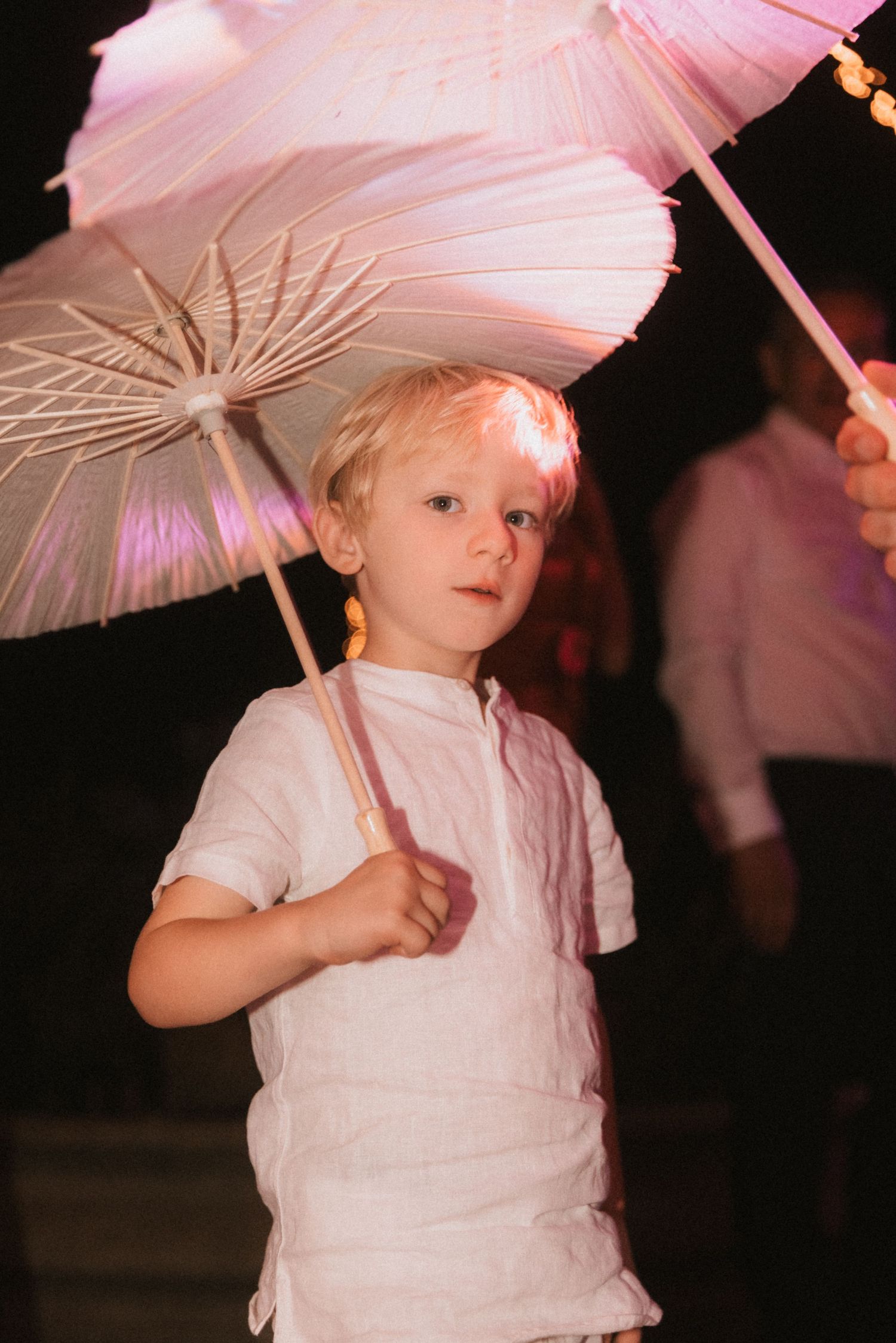 Young attendee holding a delicate pink parasol at an evening wedding celebration.
