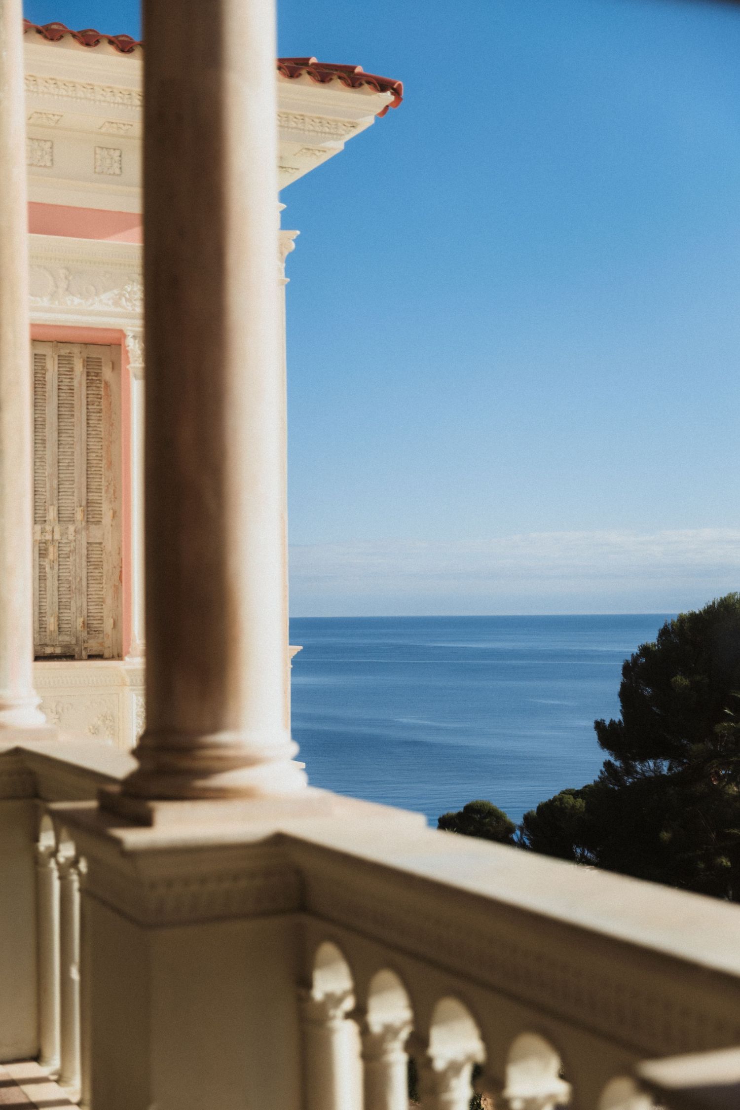 Classic Mediterranean Villa Ephrussi de Rothschild -  balcony with stone columns overlooking calm blue ocean under clear sky.