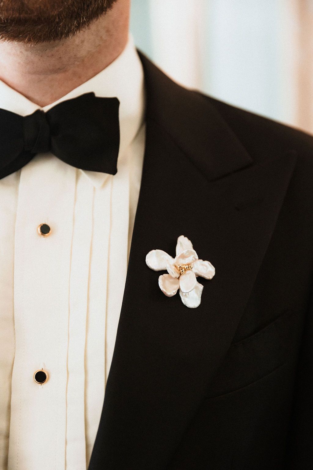 Close-up details of white bow tie boutonniere on classic black tuxedo.