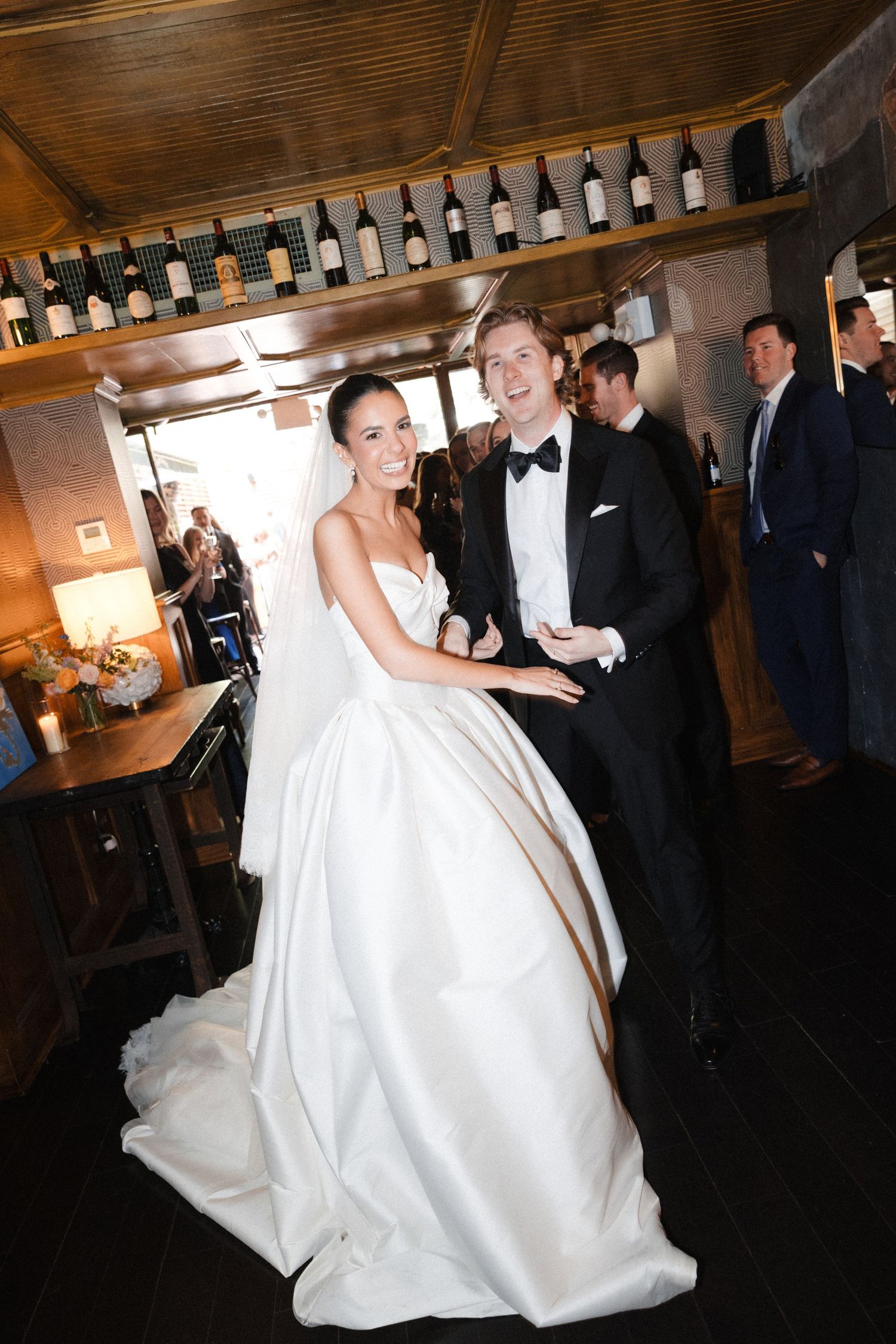 Smiling bride in strapless ball gown and groom in tuxedo posing at indoor wedding reception venue.