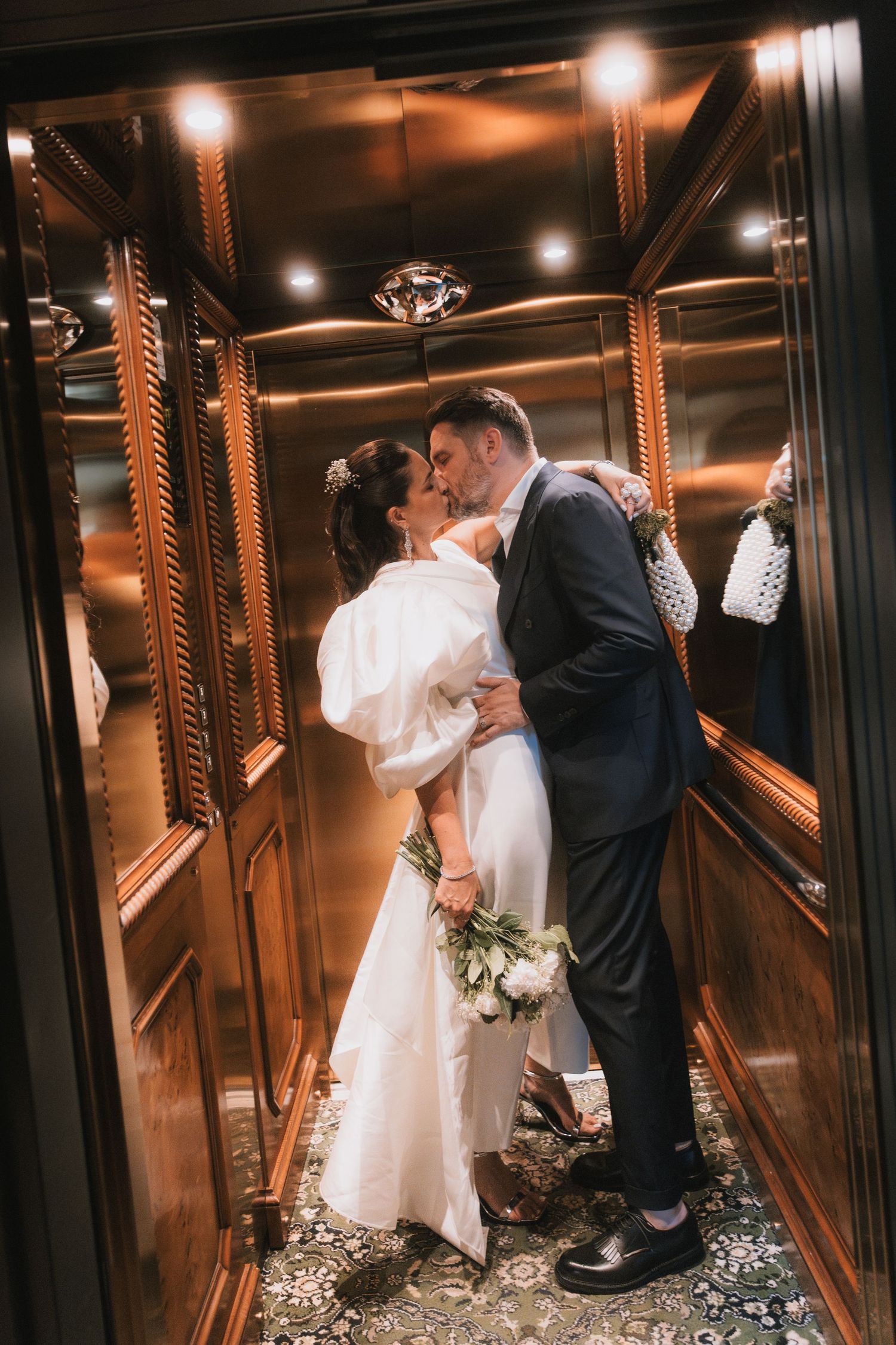 Romantic wedding moment captured in an ornate elevator with warm lighting and scattered rose petals.