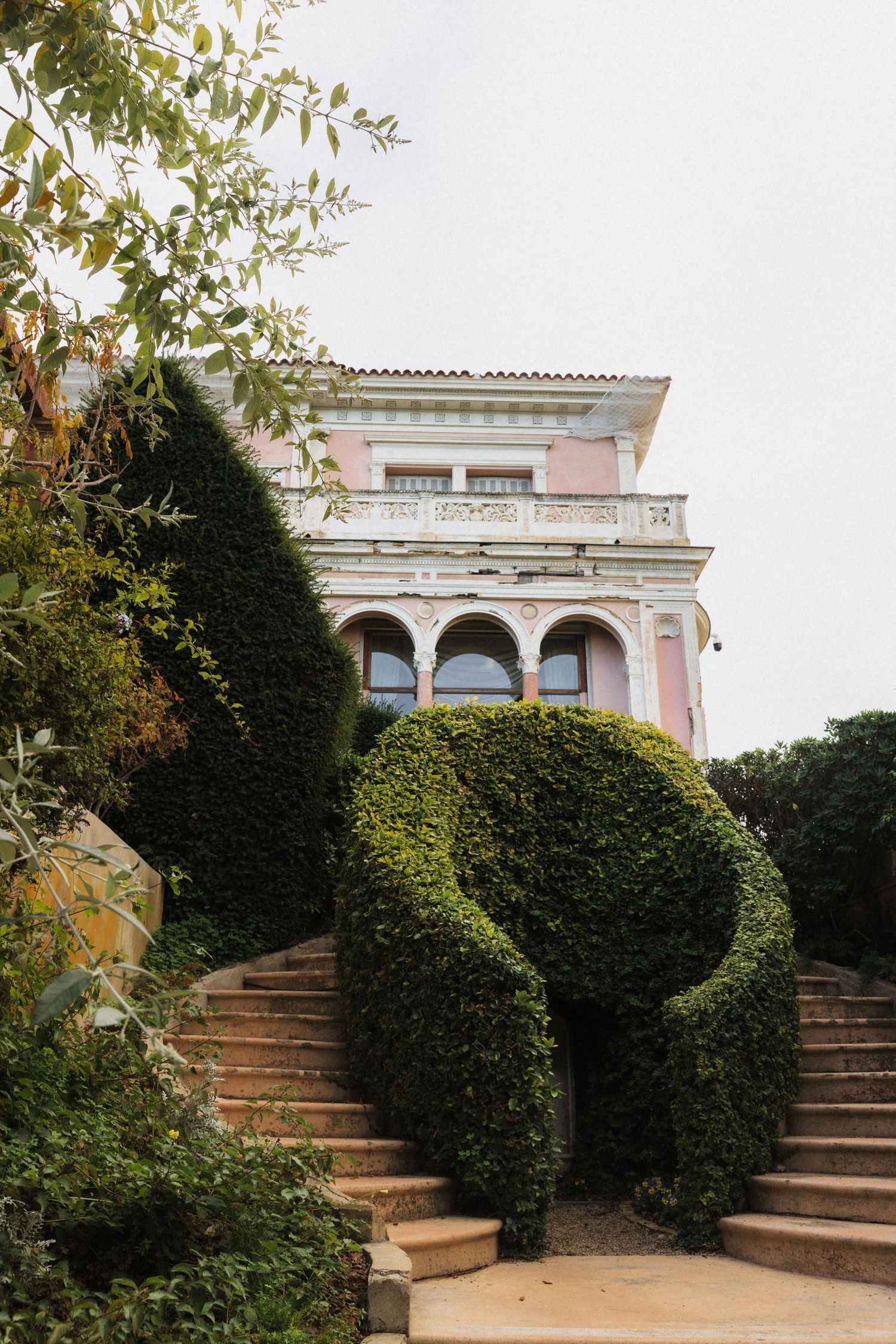 Elegant pink Mediterranean Villa Ephrussi de Rothschild with arched balconies surrounded by manicured topiary hedges in a formal garden.