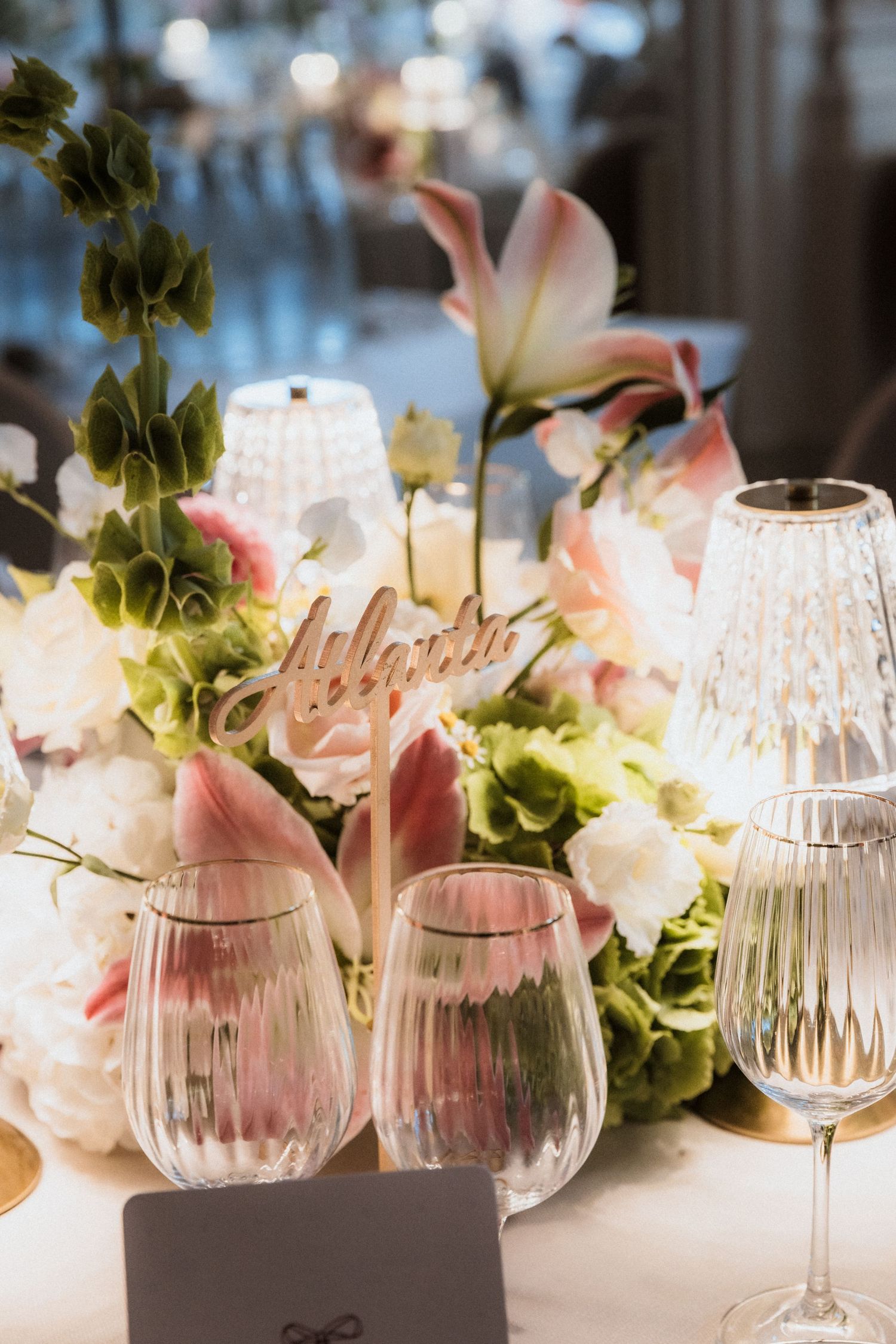 Elegant table setting with crystal wine glasses and soft pink floral arrangements in a romantic banquet setting.