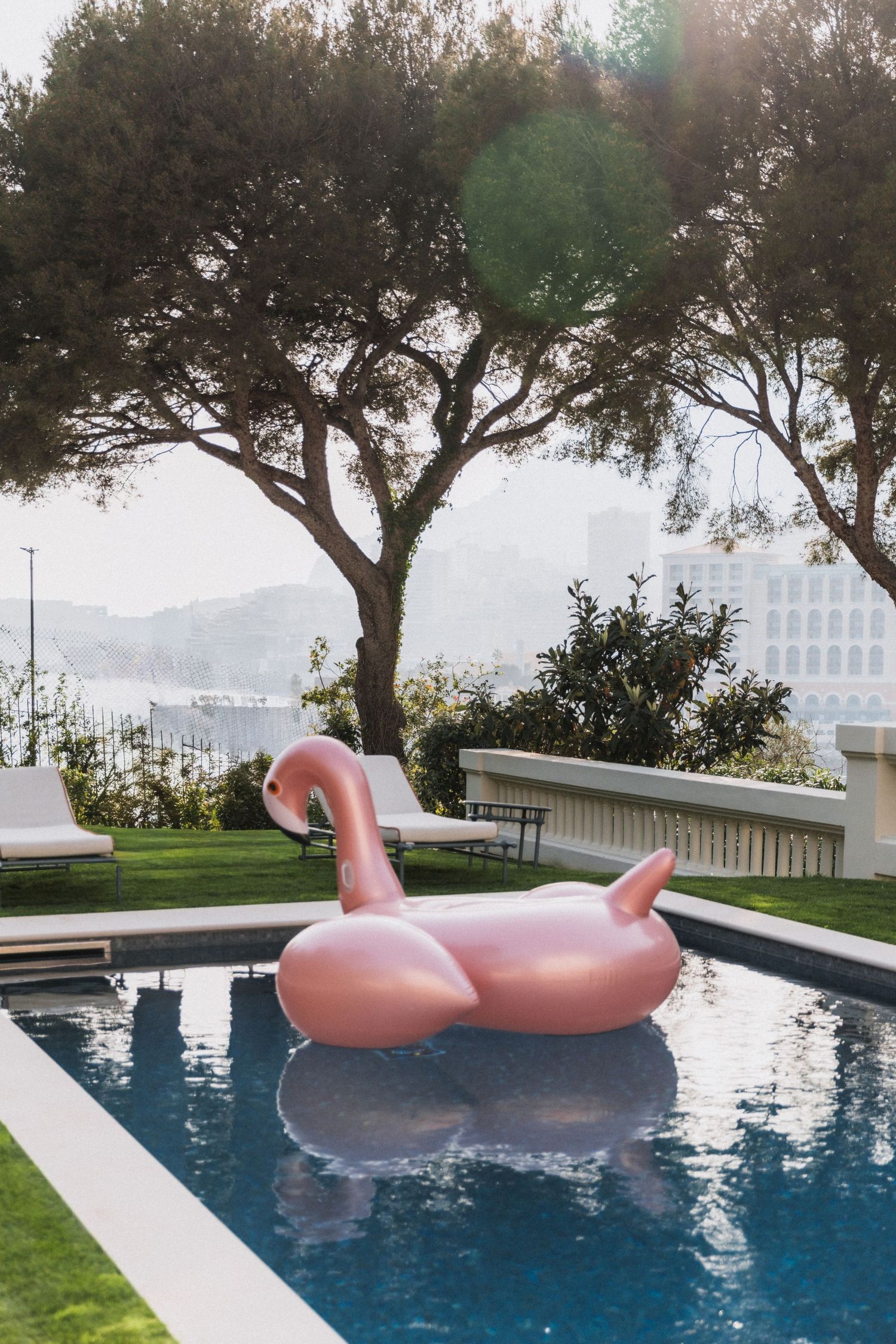 Villa La Vigie, Monaco - Pink flamingo pool float in a luxury outdoor swimming pool surrounded by lush trees with a waterfront view.