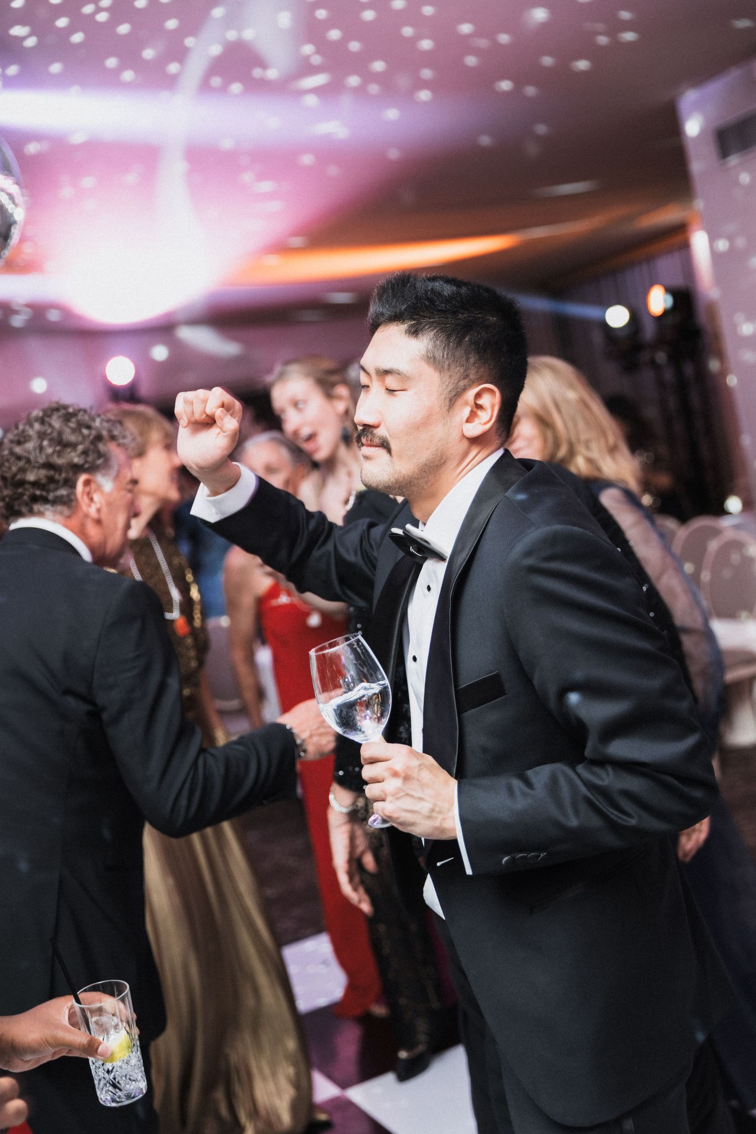Guests in tuxedos dance beneath twinkling lights at an elegant evening celebration.