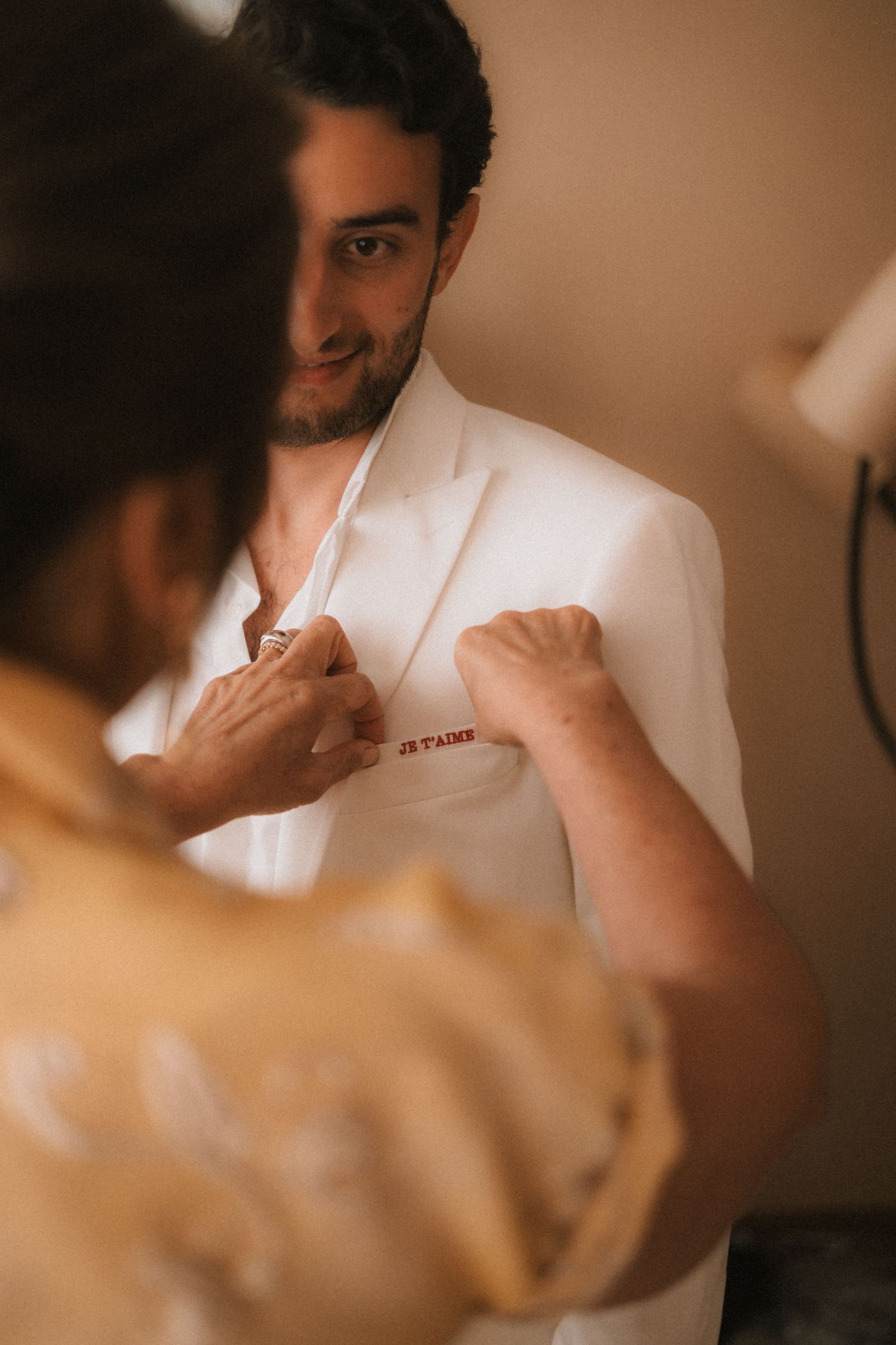 Close-up shot of someone adjusting a white suit jacket in warm lighting.