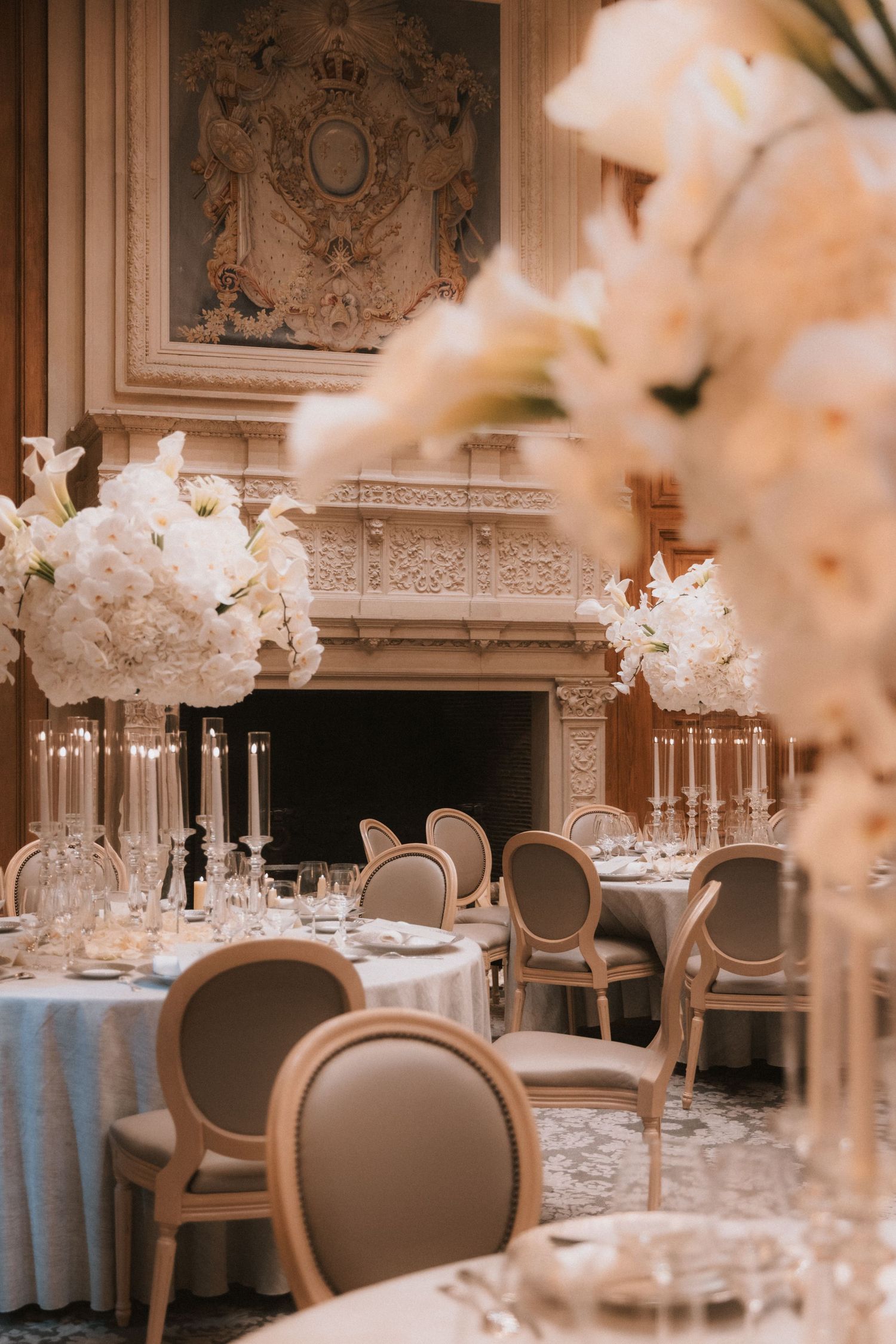 Elegant wedding reception venue with white floral centerpieces, round tables, and ornate French-style chairs in a classic ballroom.