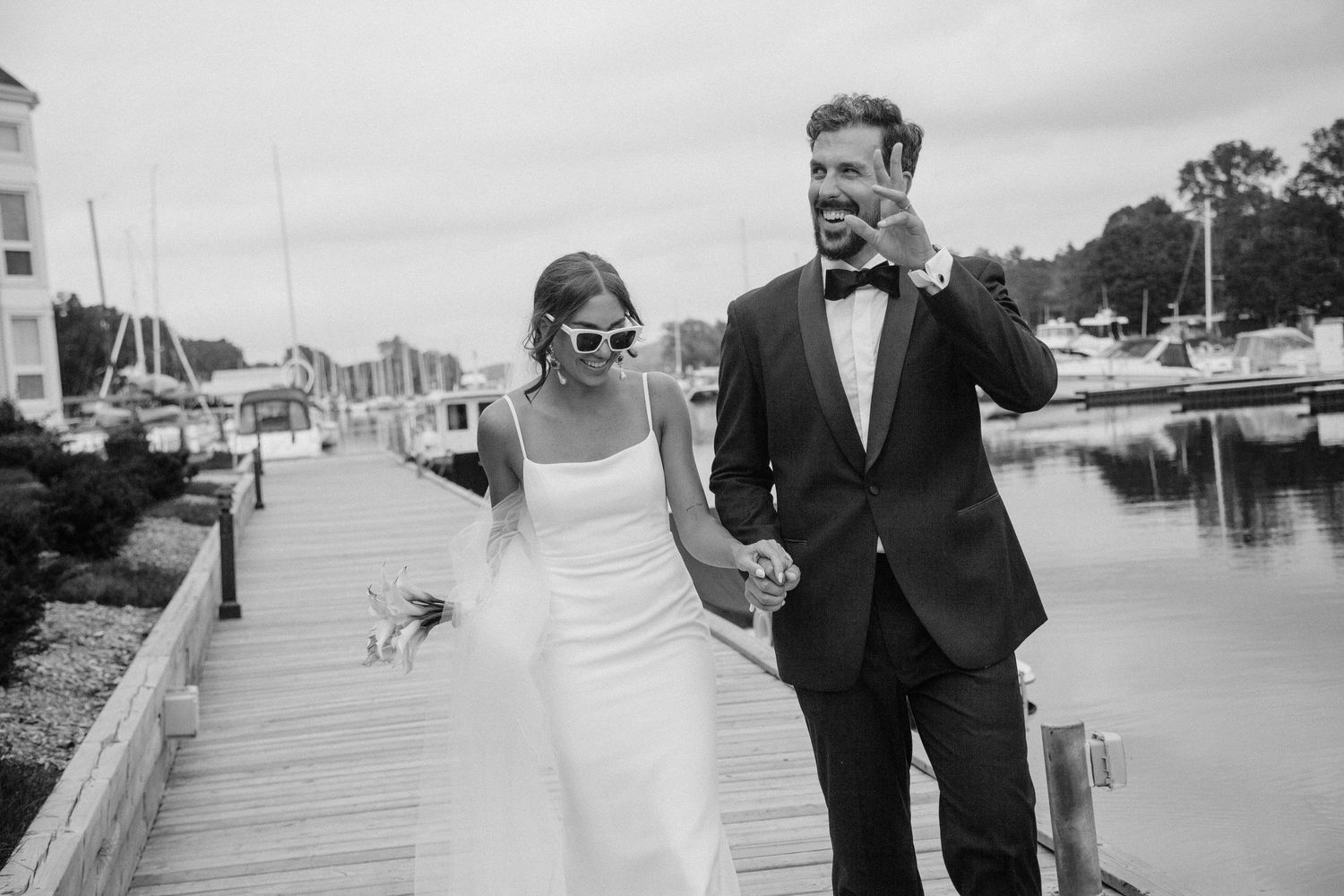 Newly married couple smile and wave from the dock at their Muskoka wedding