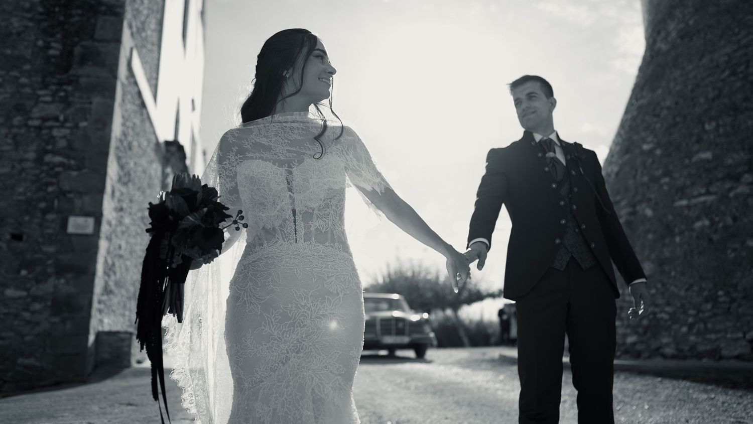 Black and white wedding photo showing silhouettes walking through a stone archway. Wedding in Jardins del Tancat, Spain.