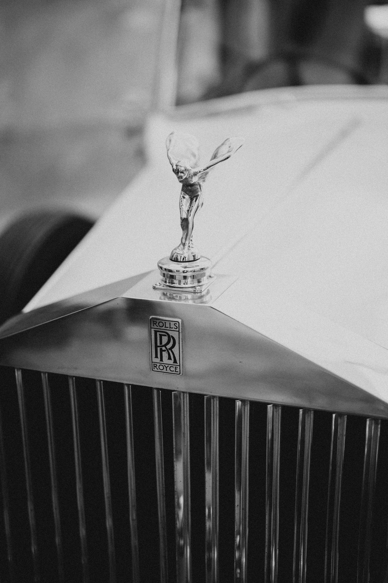 Close-up black and white photo of a Rolls-Royce Spirit of Ecstasy hood ornament on a luxury car grille. Wedding in Villa Retiro.