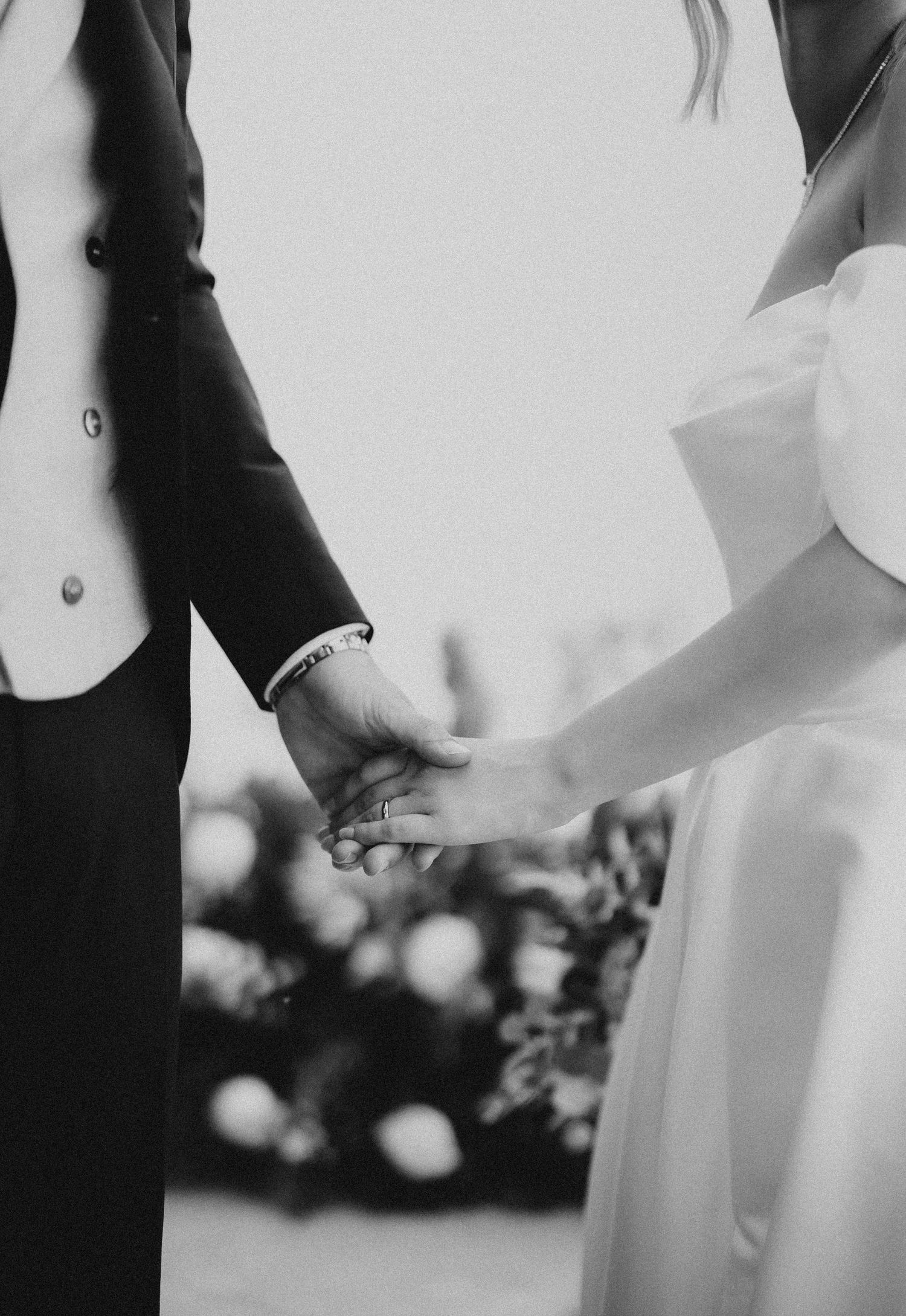 Black and white wedding photo showing couple holding hands with elegant formal attire and bouquet details. Masia Les Casotes.