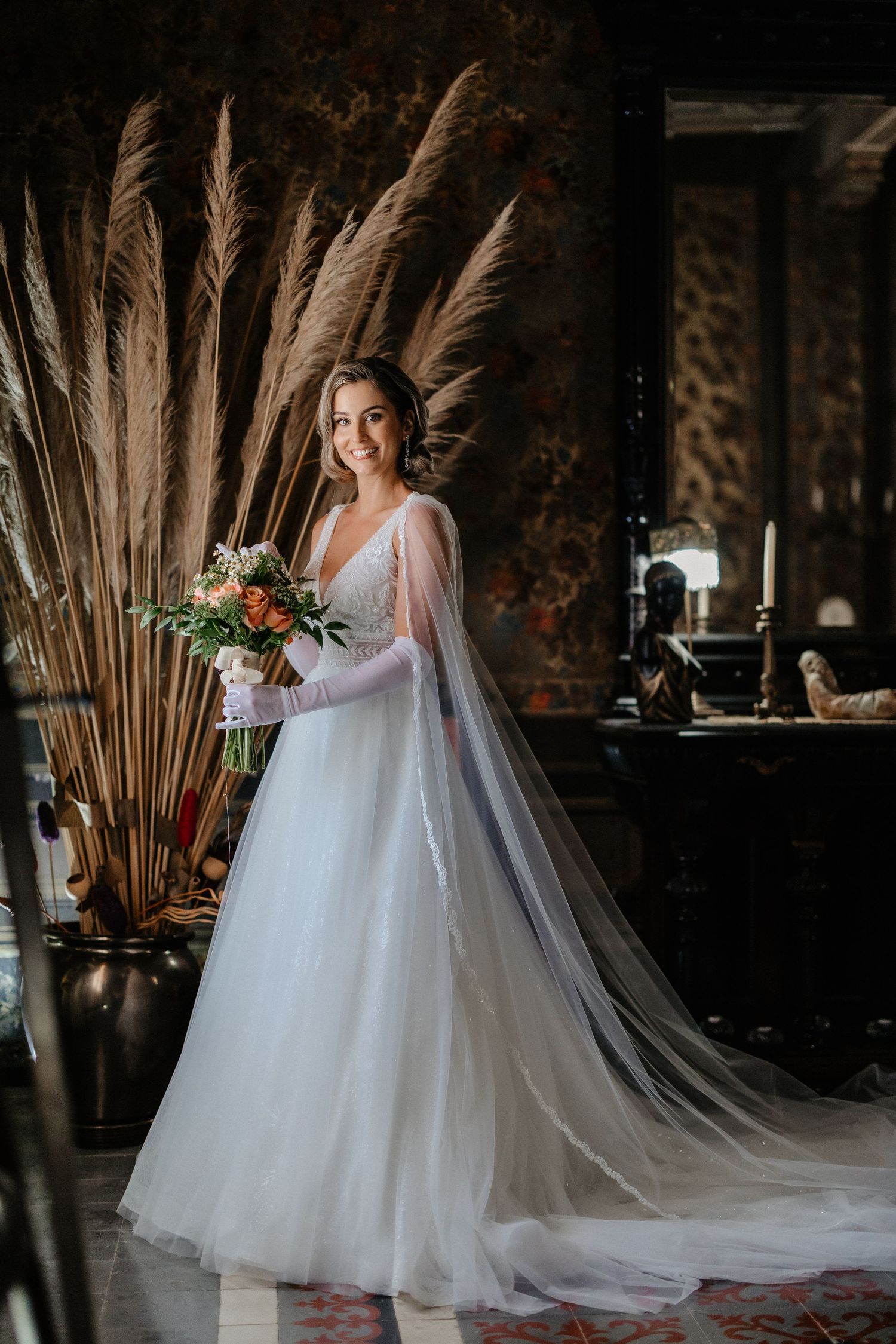 A bride in a flowing white tulle wedding gown poses in a rustic venue with pampas grass and natural decor. Wedding in Villa Retiro.