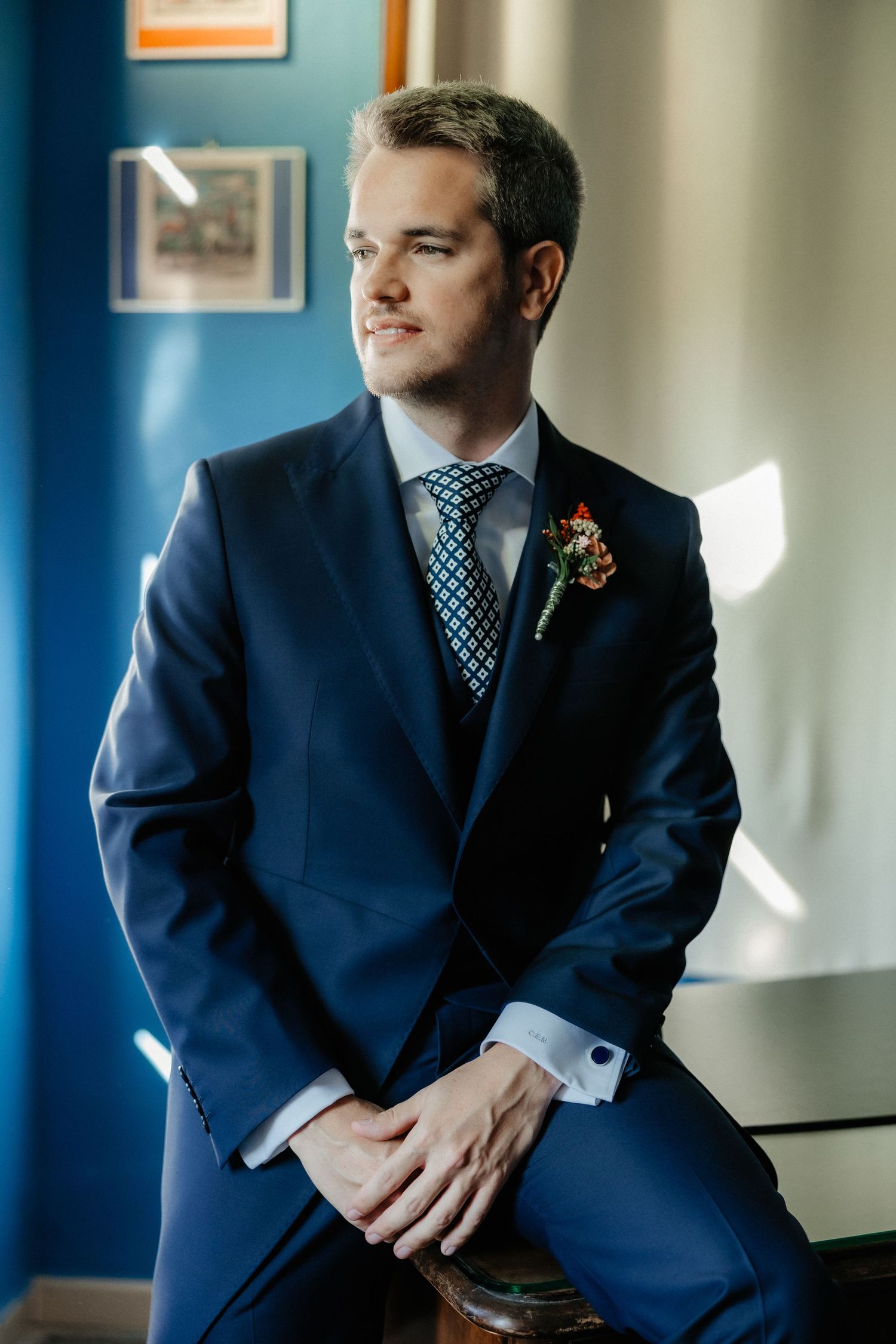 Professional in a navy blue suit sits thoughtfully in an office setting with blue walls and natural lighting. Wedding in Villa Retiro.