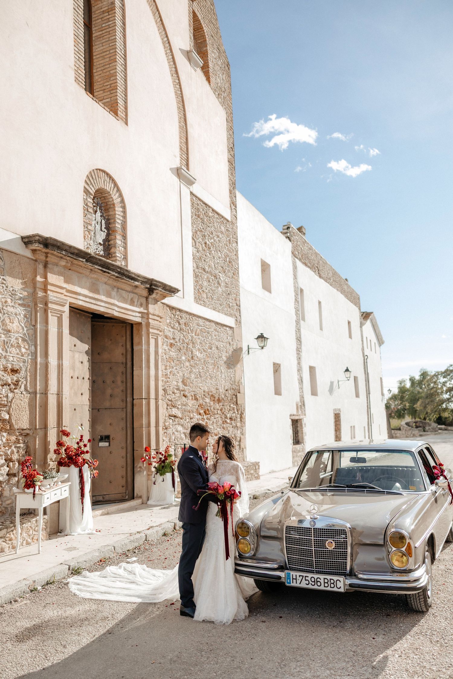 A classic vintage Mercedes-Benz car parked outside a rustic white church building with stone walls. Wedding in Jardins del Tancat.