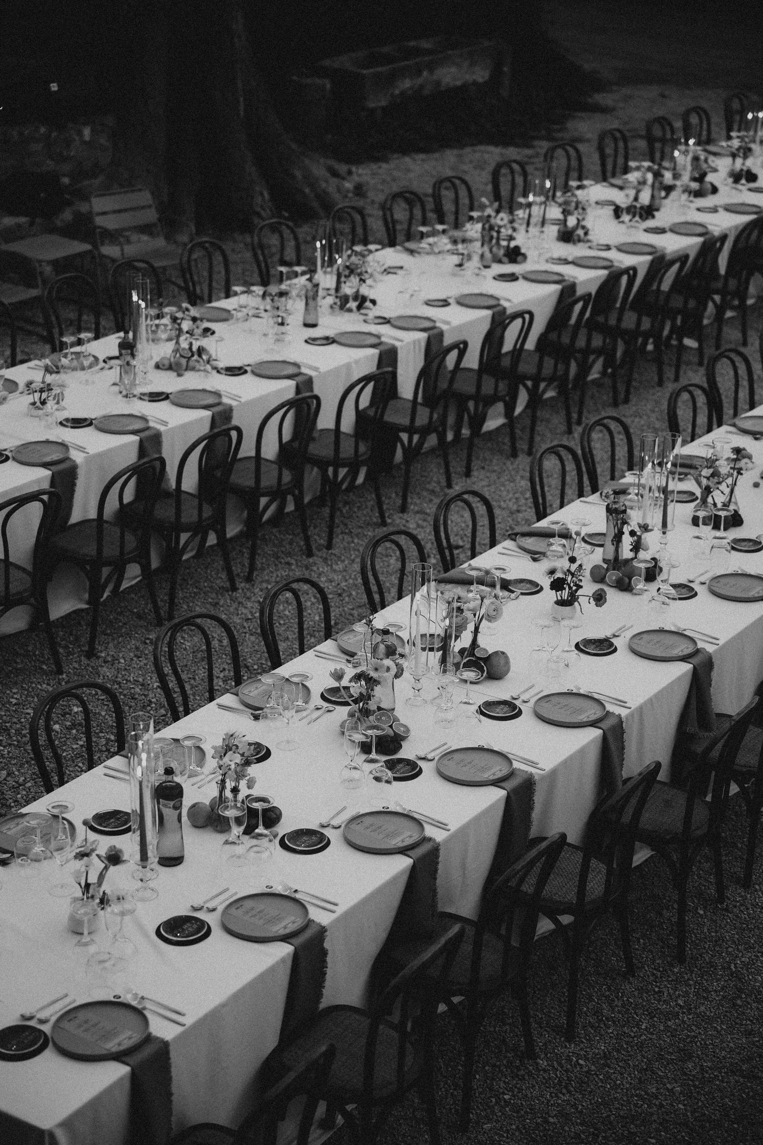 Banquet tables set with white linens, place settings and chairs stretch into the distance in a black and white photograph.  Mas de l'Ila.