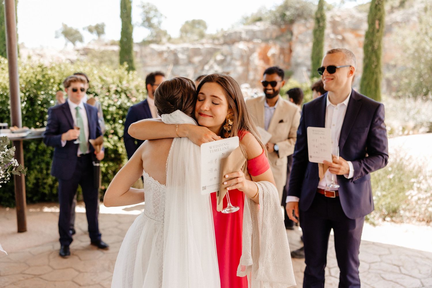 Wedding guests share warm embraces and celebrate at an outdoor venue with cypress trees in the background. Wedding in Les Moles.