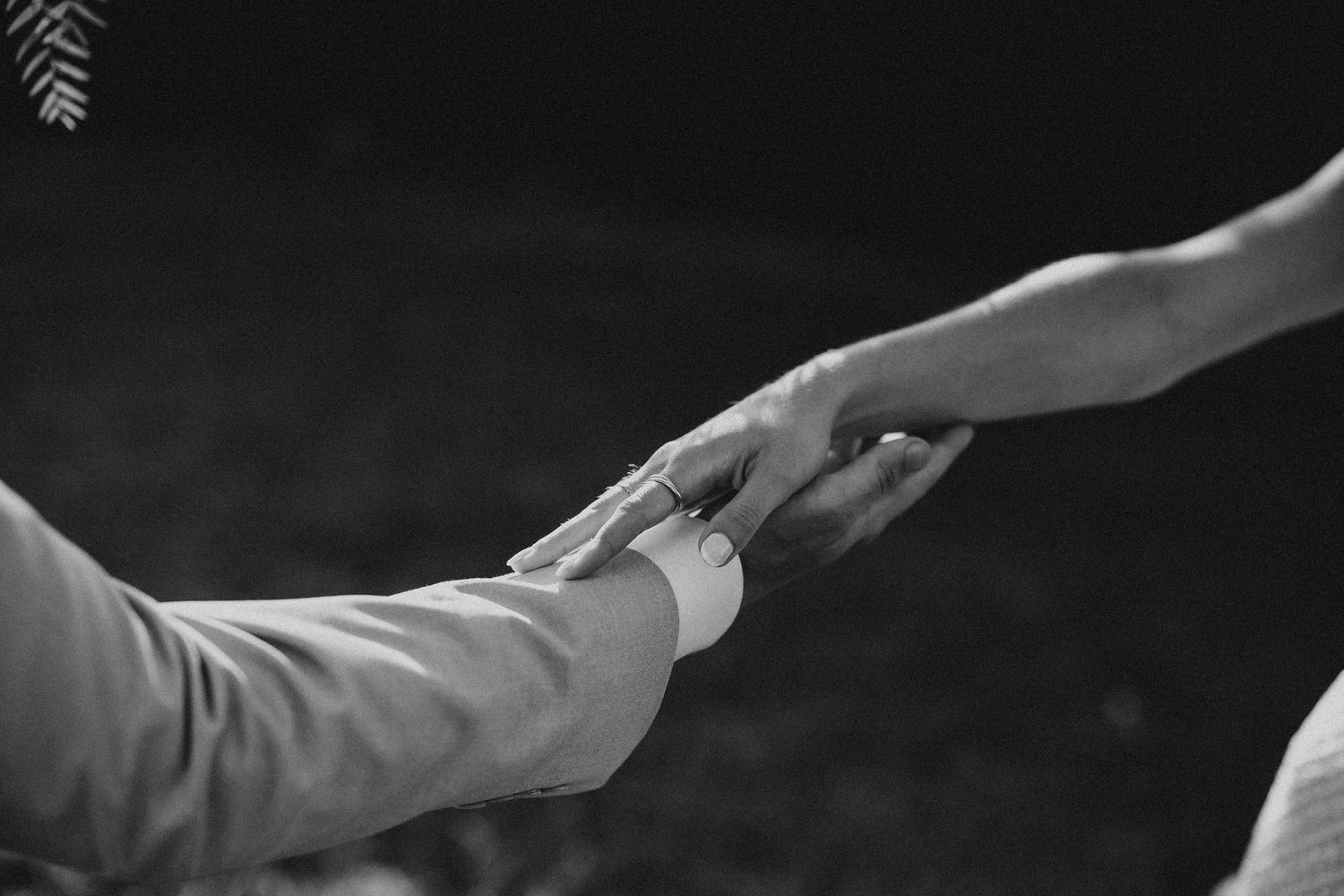 Two hands reach toward each other dramatically in black and white against a dark background. Wedding in Les Moles.