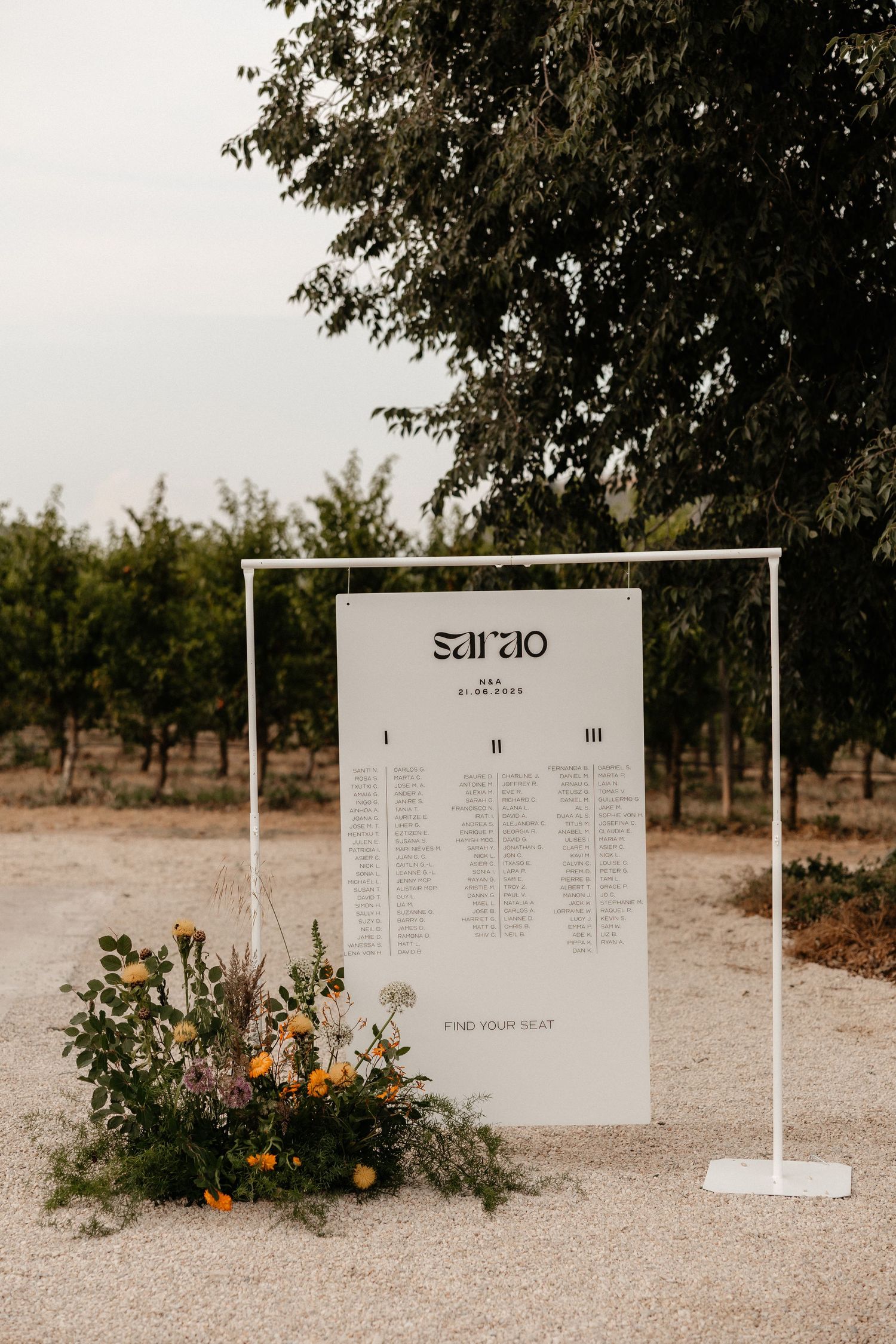 Modern wedding seating chart displays with white boards and floral arrangements in an outdoor orchard setting.  Wedding in Mas de l'Illa.