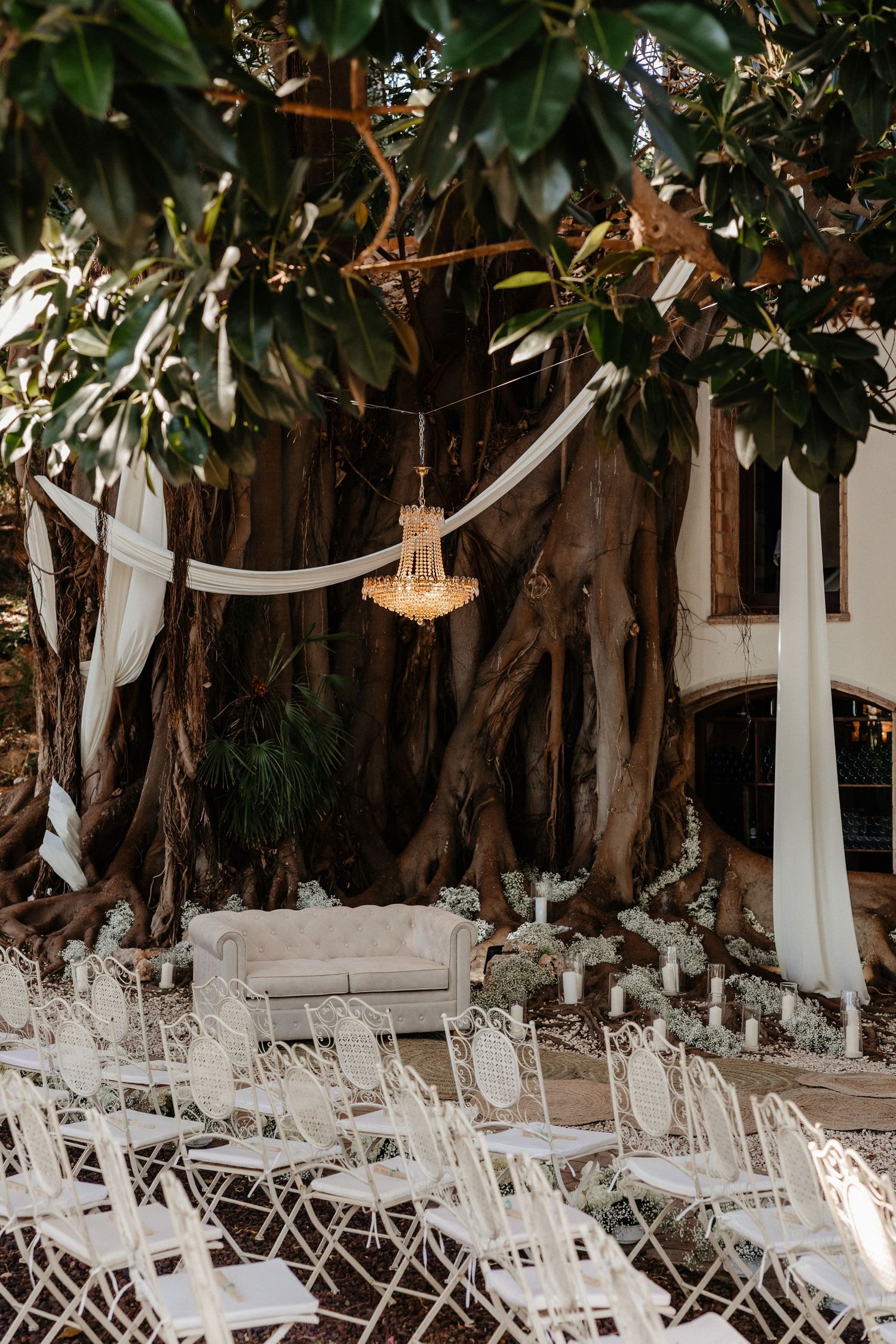 White folding chairs arranged for an outdoor wedding ceremony under draped fabric and lush greenery canopy.  Wedding in Villa Retiro.
