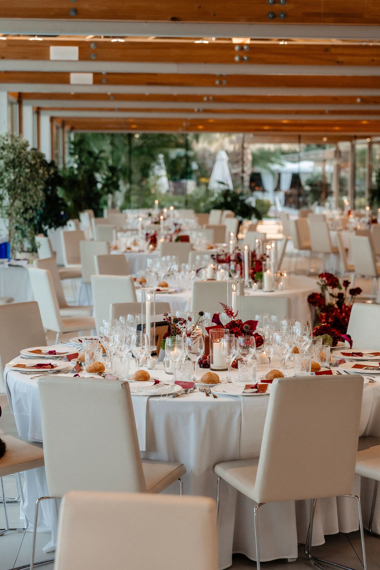 Elegant wedding reception venue with round tables decorated in white linens and burgundy floral centerpieces. Wedding in Jardins del Tancat.