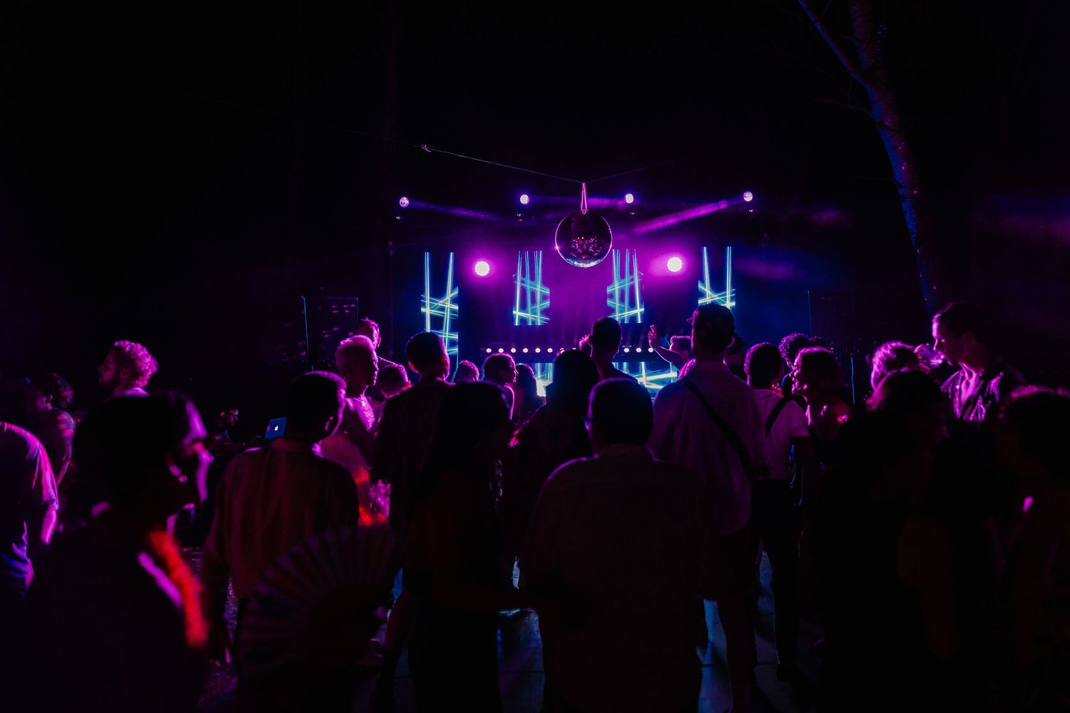 A dark nightclub scene illuminated by purple lights with silhouettes of people dancing on a crowded dance floor. Mas de l'Illa.