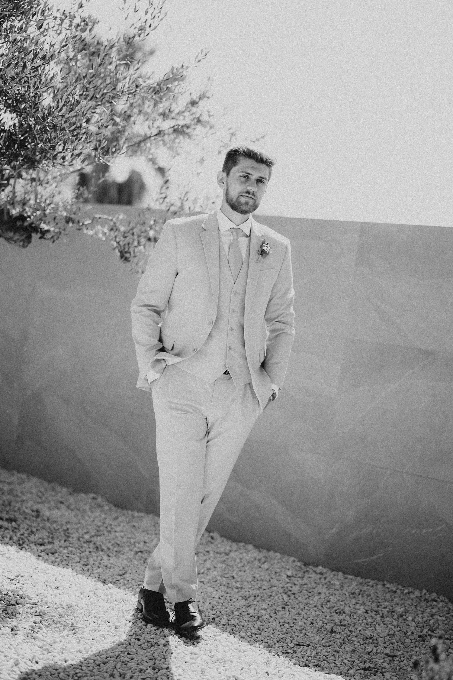 A series of black and white photos showing a person in a light-colored suit posing against a wall outdoors. Wedding in Les Moles.