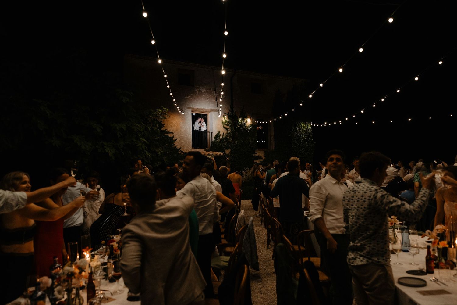 Wedding guests dance together under twinkling string lights at an outdoor evening reception. Mas de l'Illa.