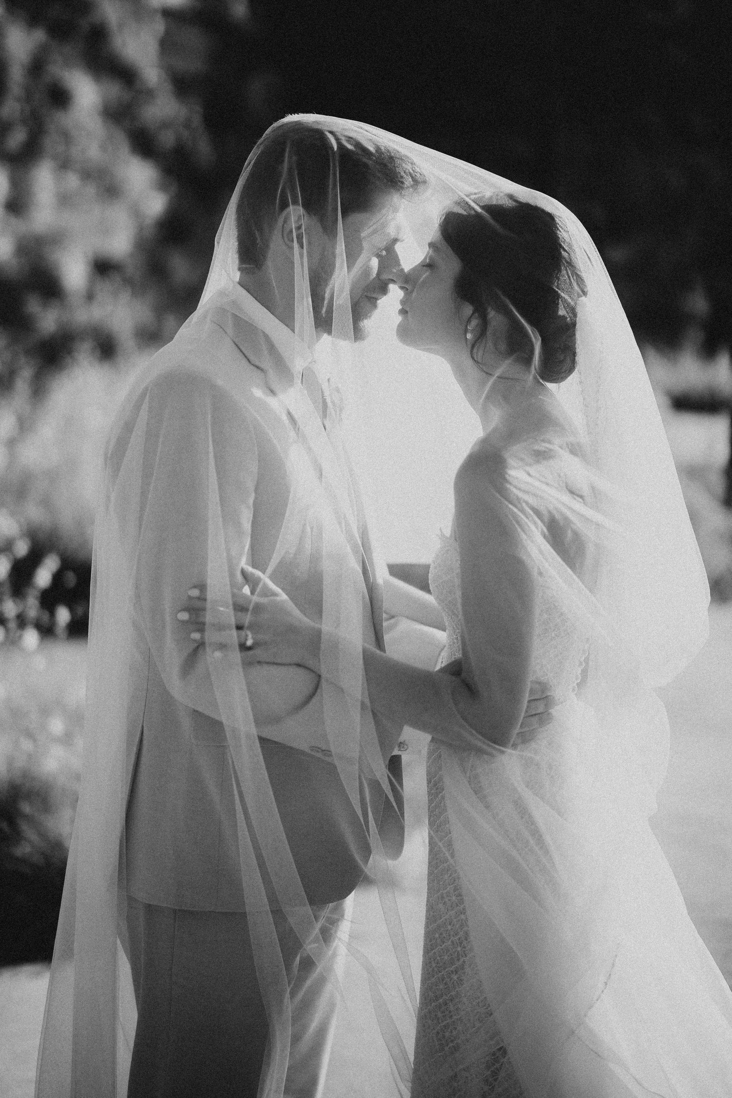 A romantic black and white wedding photo showing a couple sharing an intimate moment under a flowing veil. Wedding in Les Moles.