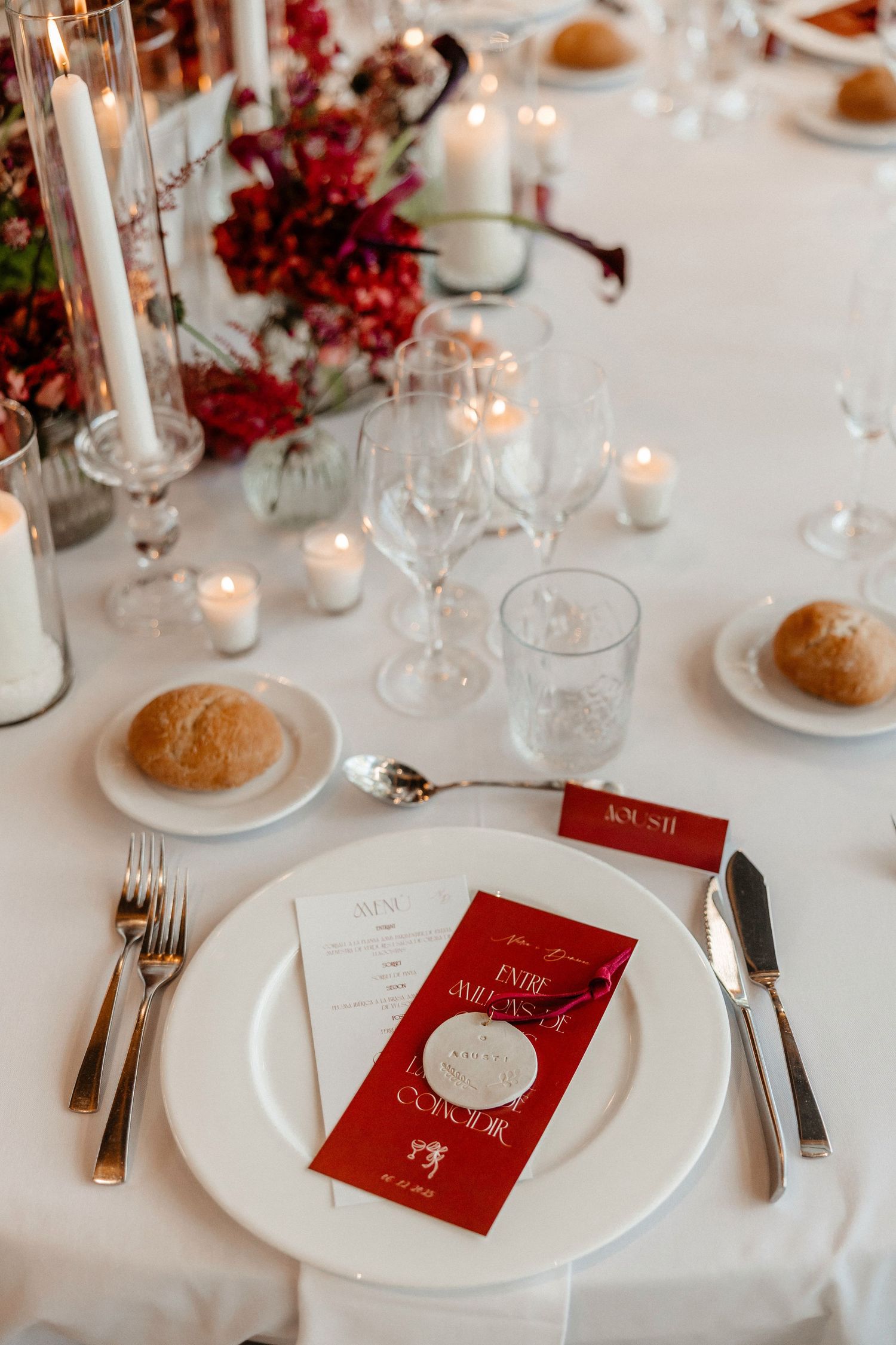 Elegant table settings with white plates, red menus, and glowing candles create a romantic holiday atmosphere. Wedding in Jardins del Tancat