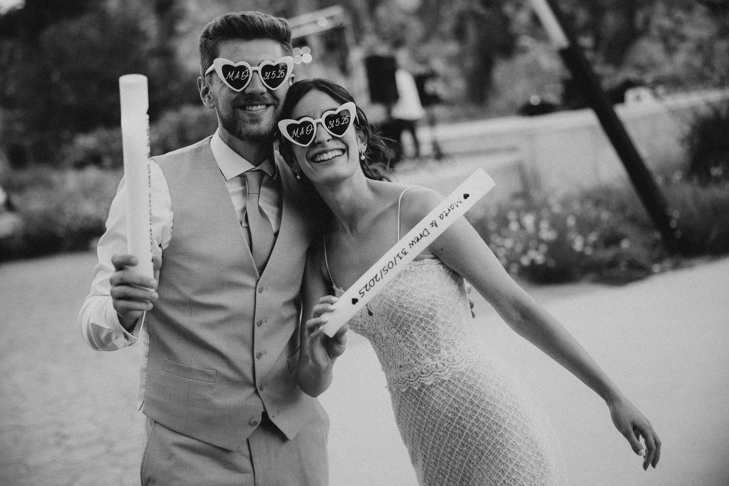 A happy couple in sunglasses poses together at their wedding celebration, both holding up white bottles. Wedding in Les Moles.