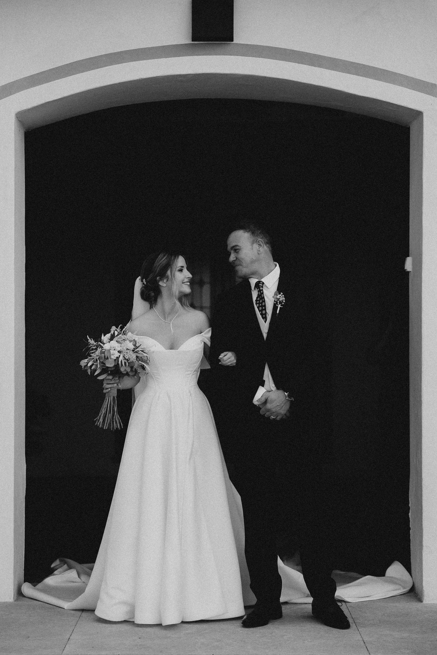 Black and white wedding photo series showing couple in formal attire against arched architectural backdrop. Wedding in Masia Les Casotes.