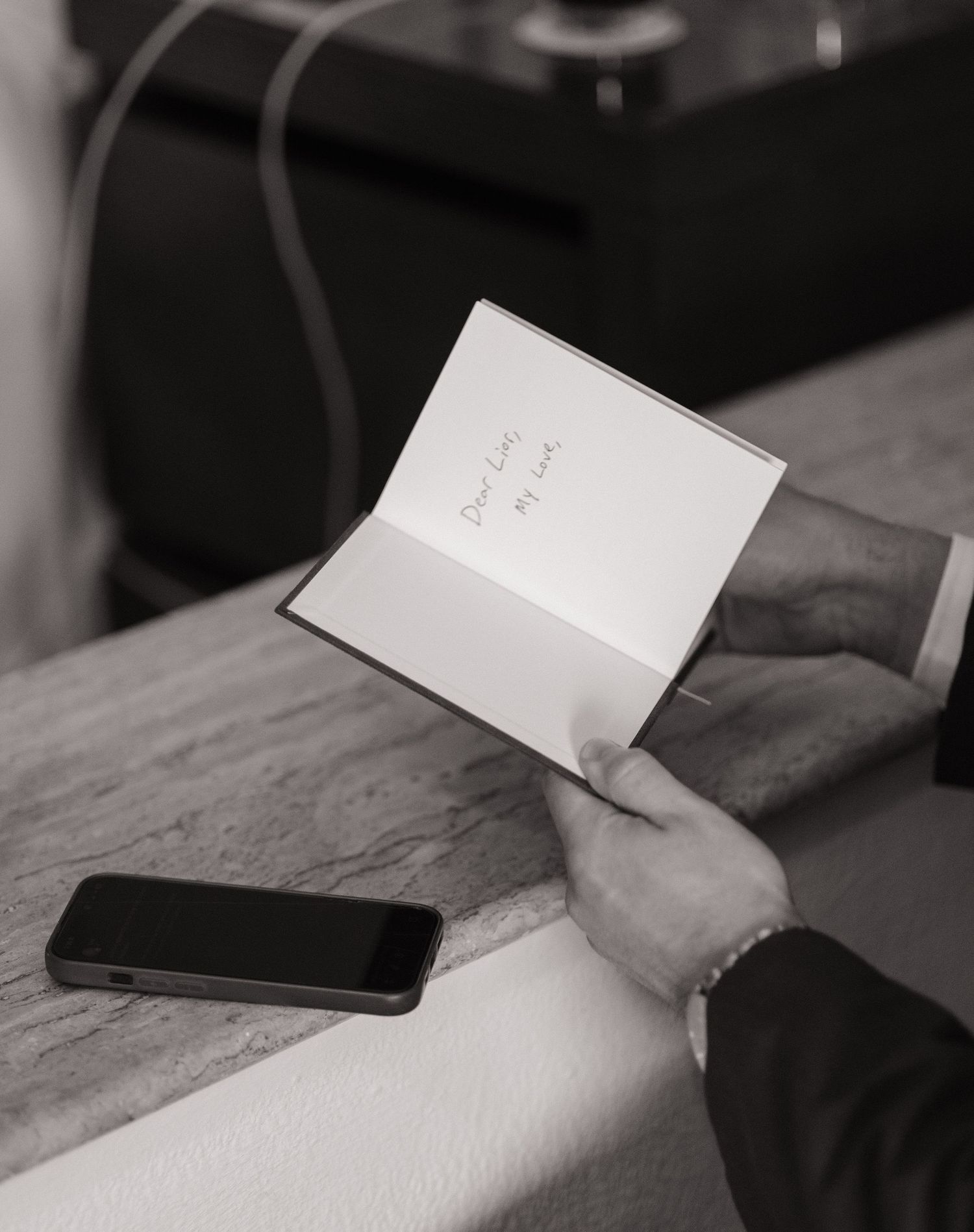 A hand holding an open white card or note with a mobile phone on a wooden surface.