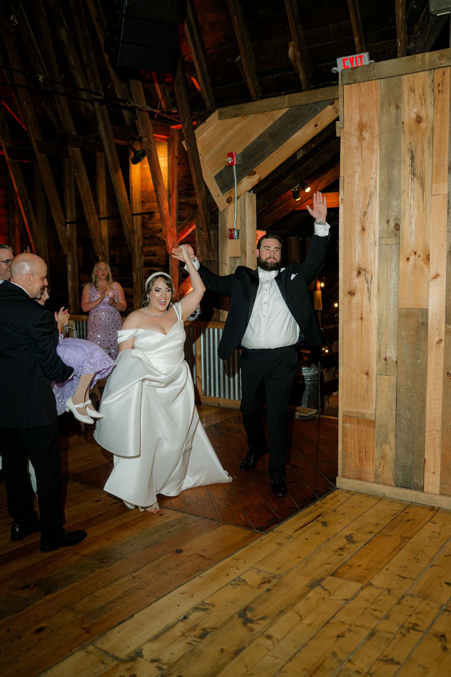 Newlyweds make grand entrance into rustic wooden barn venue with raised arms in celebration.