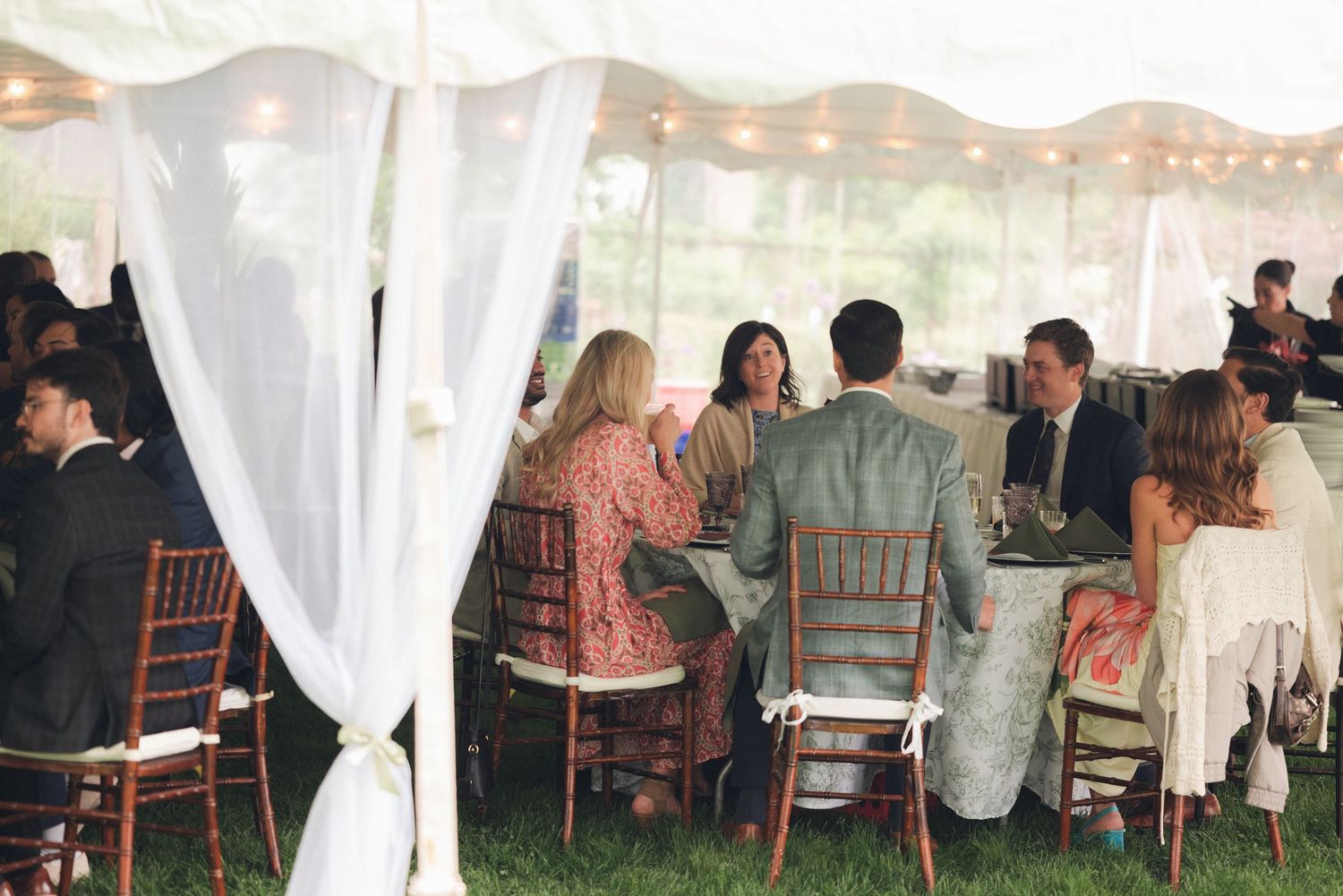 Guests dining under a white tent with string lights at an elegant outdoor wedding reception.
