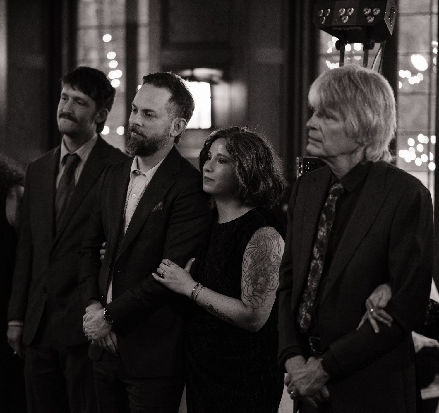 Black and white photo of four people standing together at a formal event, including a woman with a tattoo.