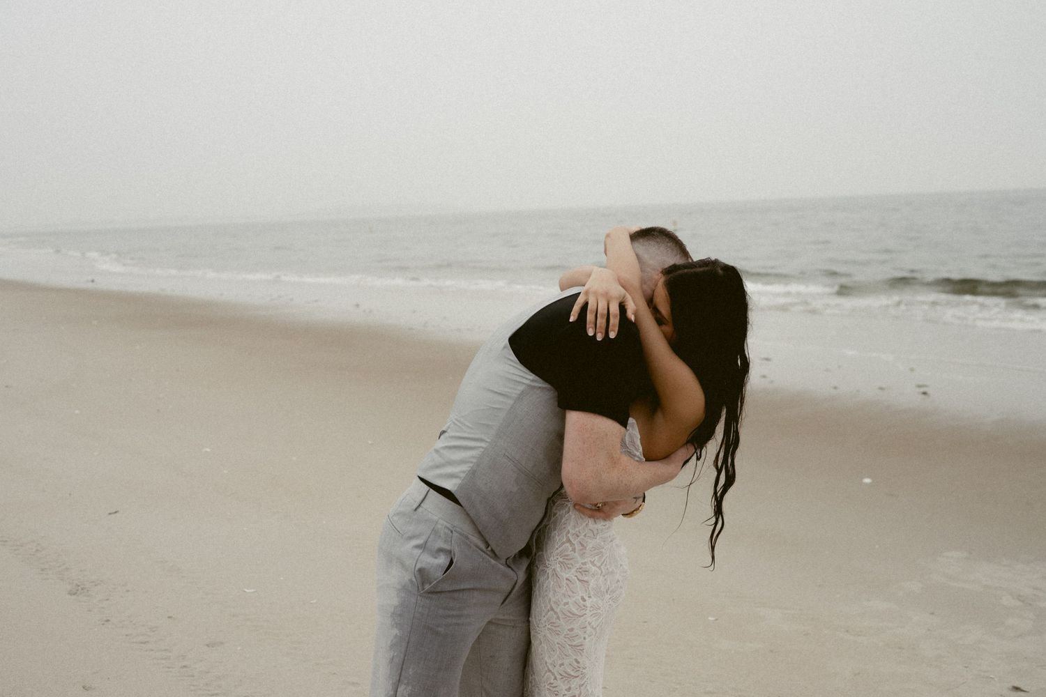 A couple embraces on a misty beach with waves crashing in the background.