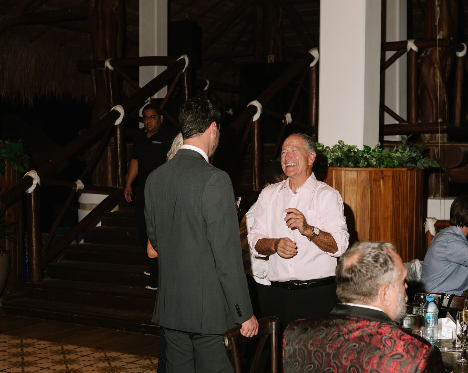 Two people having an animated conversation at an indoor gathering with wooden canes displayed in the background.