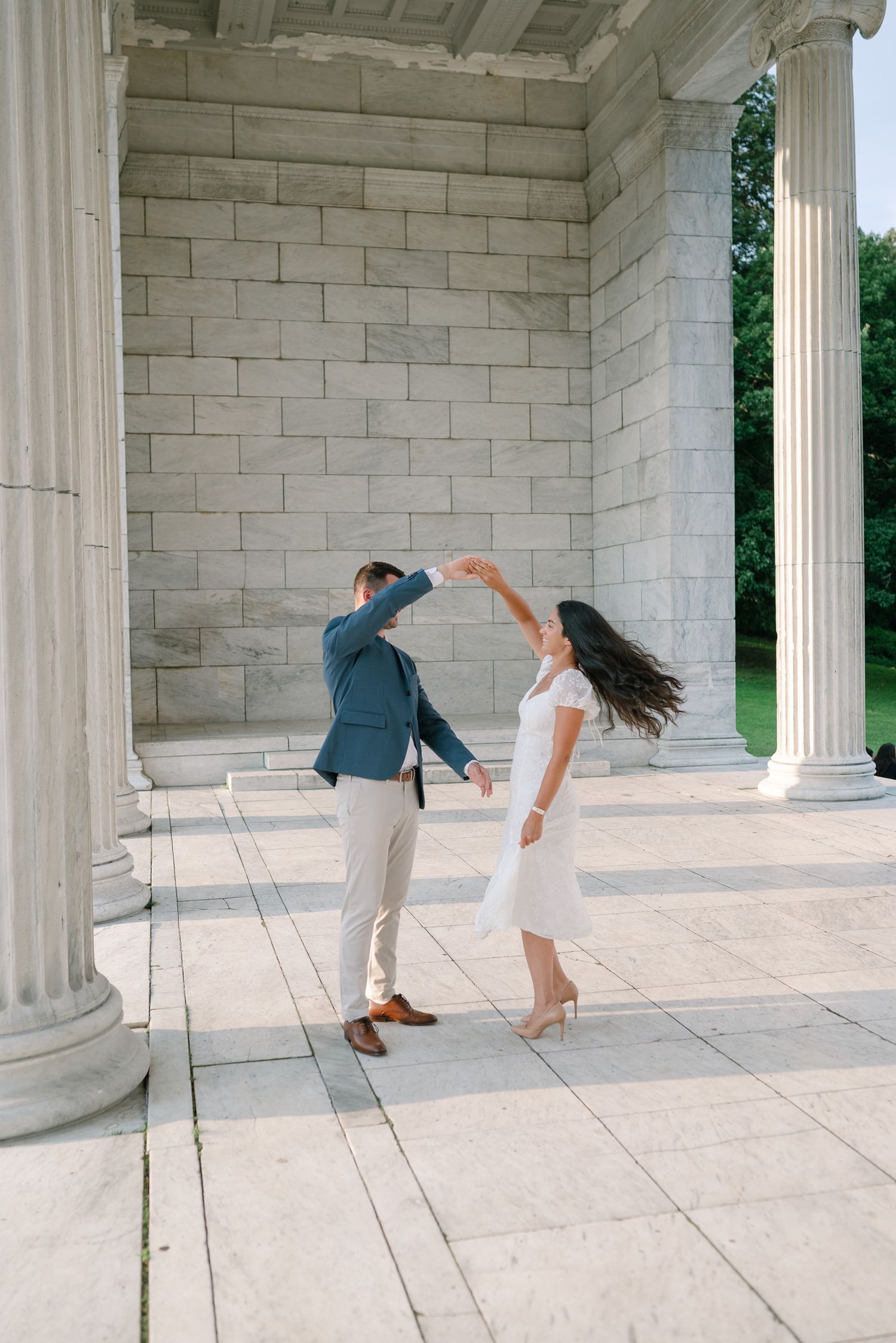 Dancing couple captured in motion between white marble columns during photo shoot.