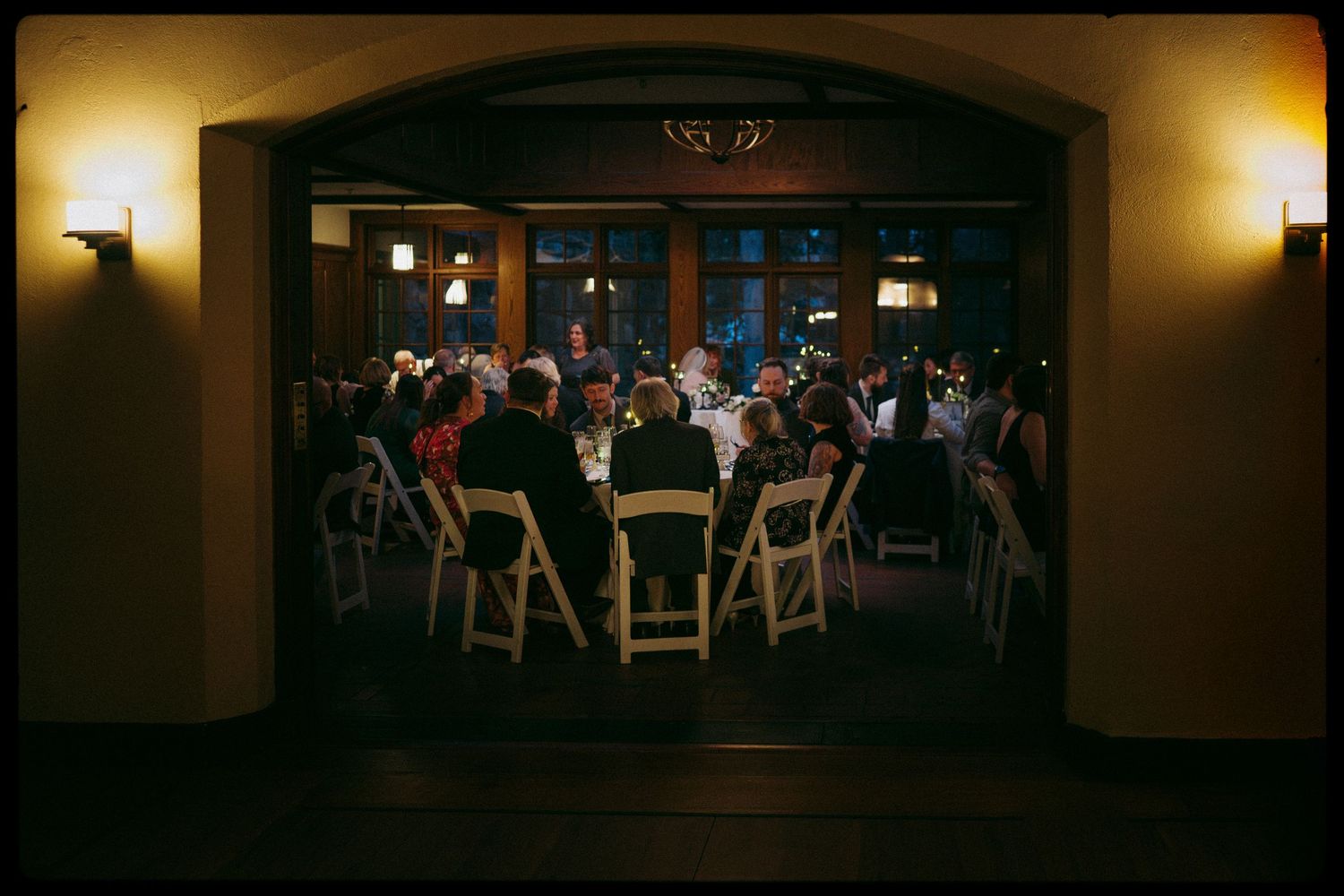 Guests seated at round tables during an elegant evening wedding reception viewed through a grand archway.