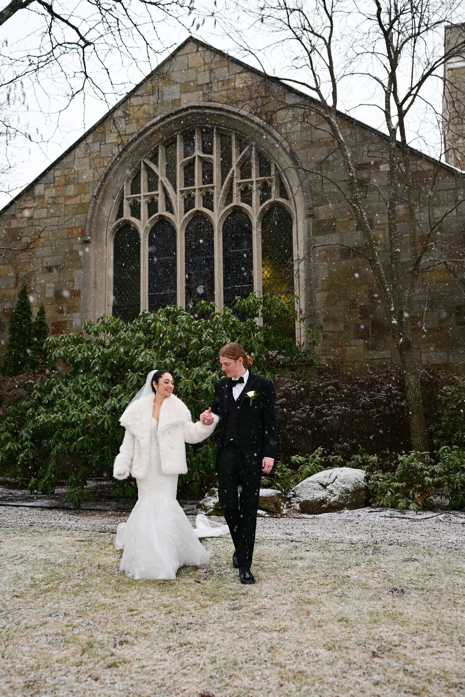 Winter wedding photos being taken outside a gothic stone church with snow on the ground.