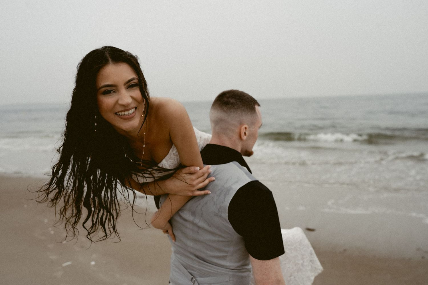 Playful couple enjoying a romantic photoshoot on a cloudy beach with waves in the background.